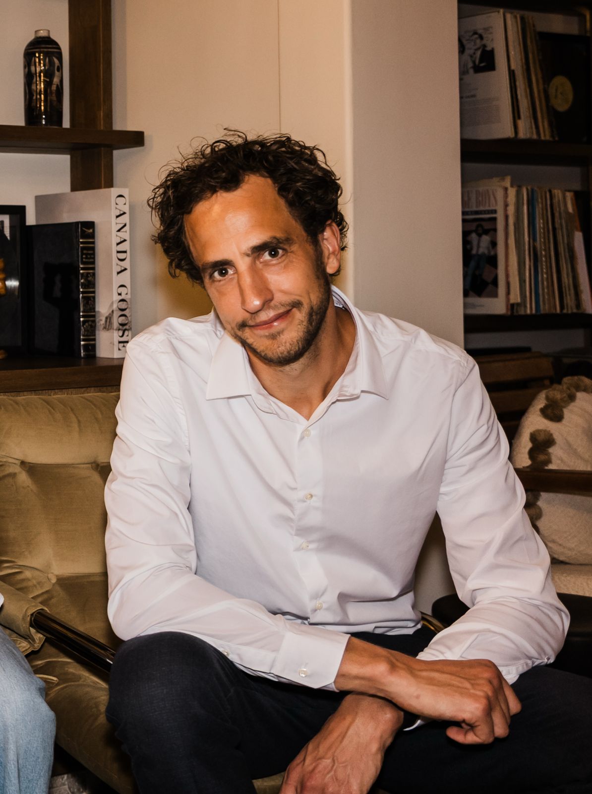 A woman with a white headband relaxing, her face illuminated by warm sunlight filtering through blinds, casting striped shadows. She has a serene and peaceful expression.