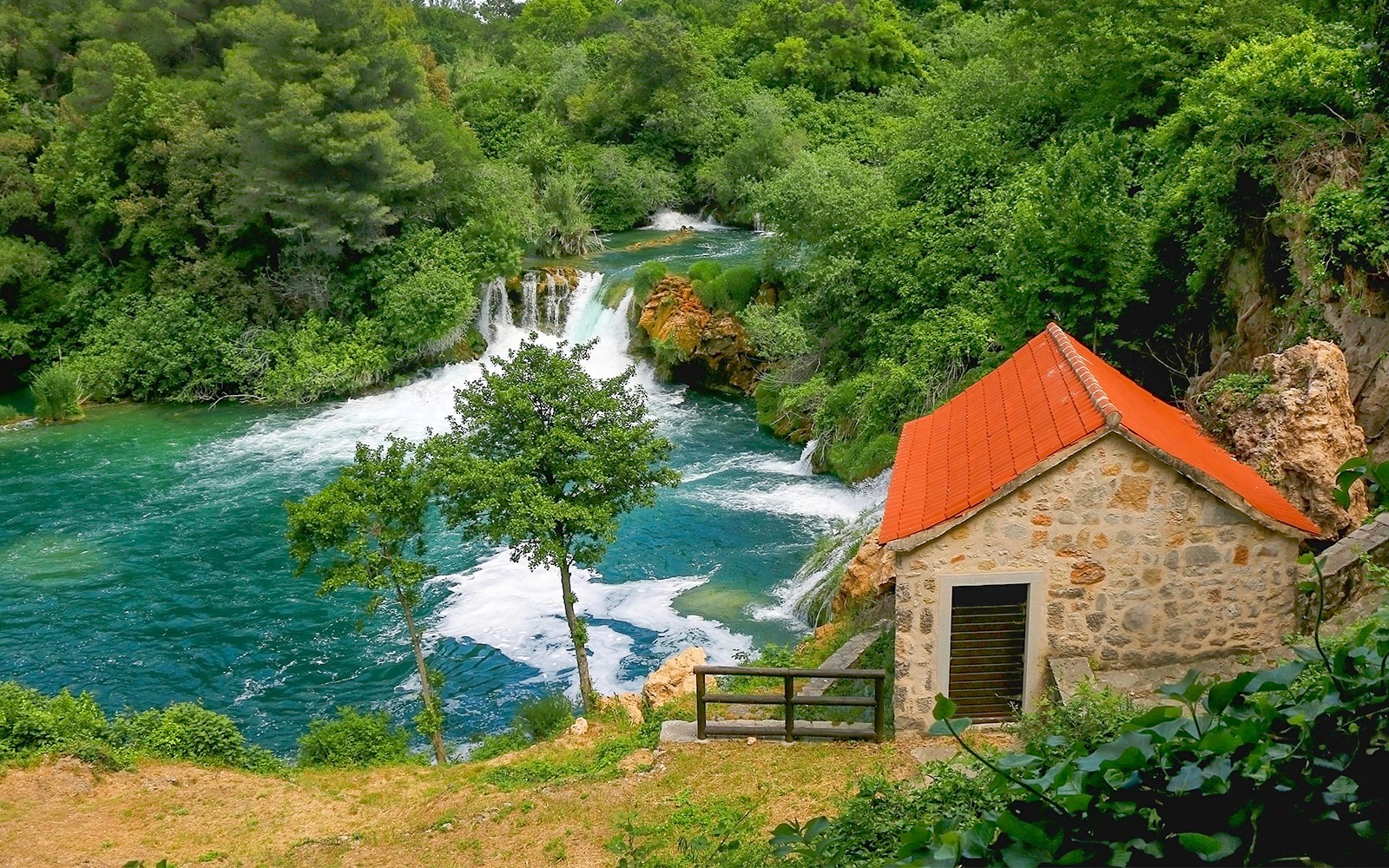 Vattenfall och stenhus vid Krka Nationalpark i Kroatien, omgivet av frodig grönska.