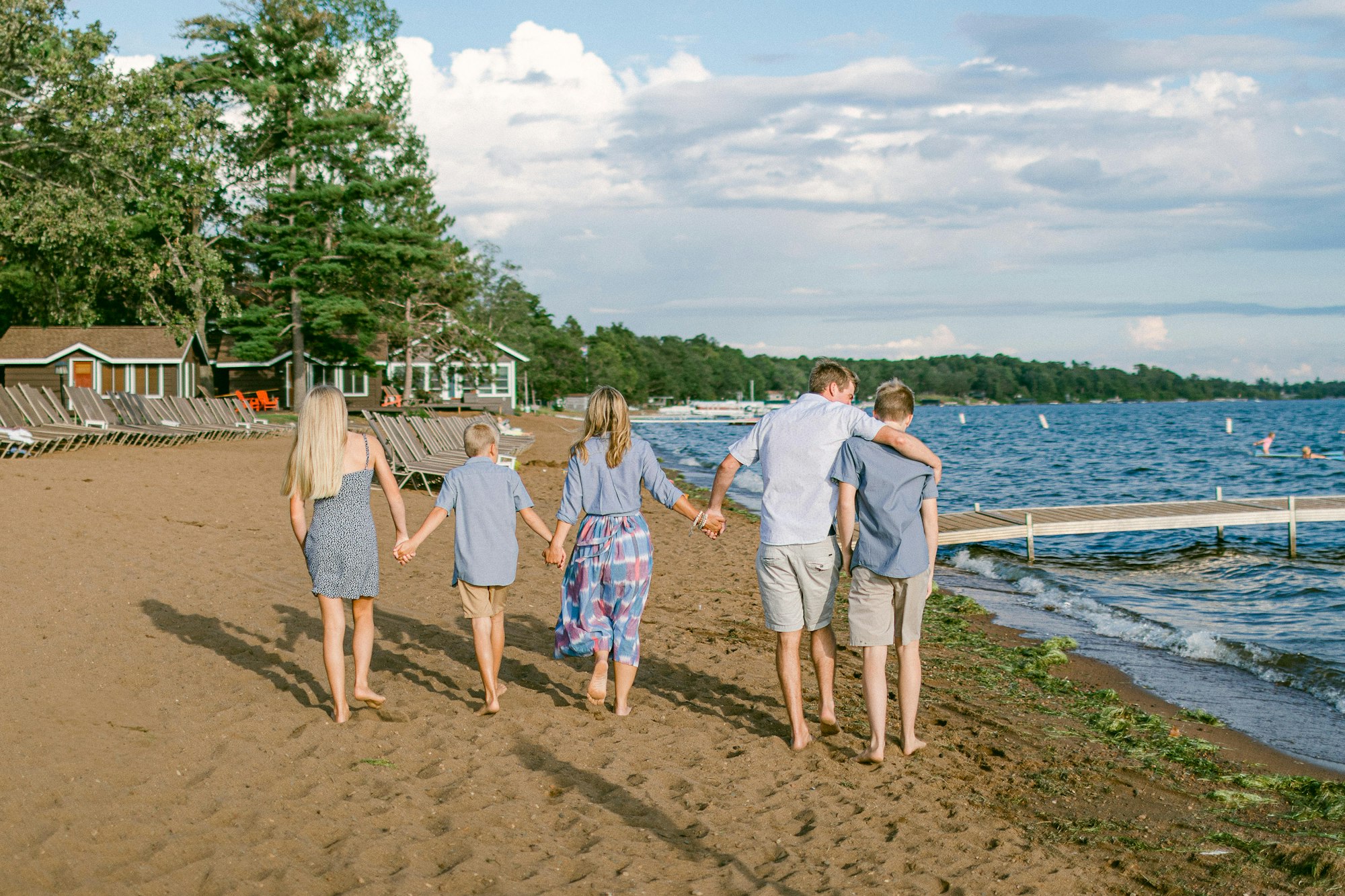 A family of five walking hand in hand along a sandy beach toward the water