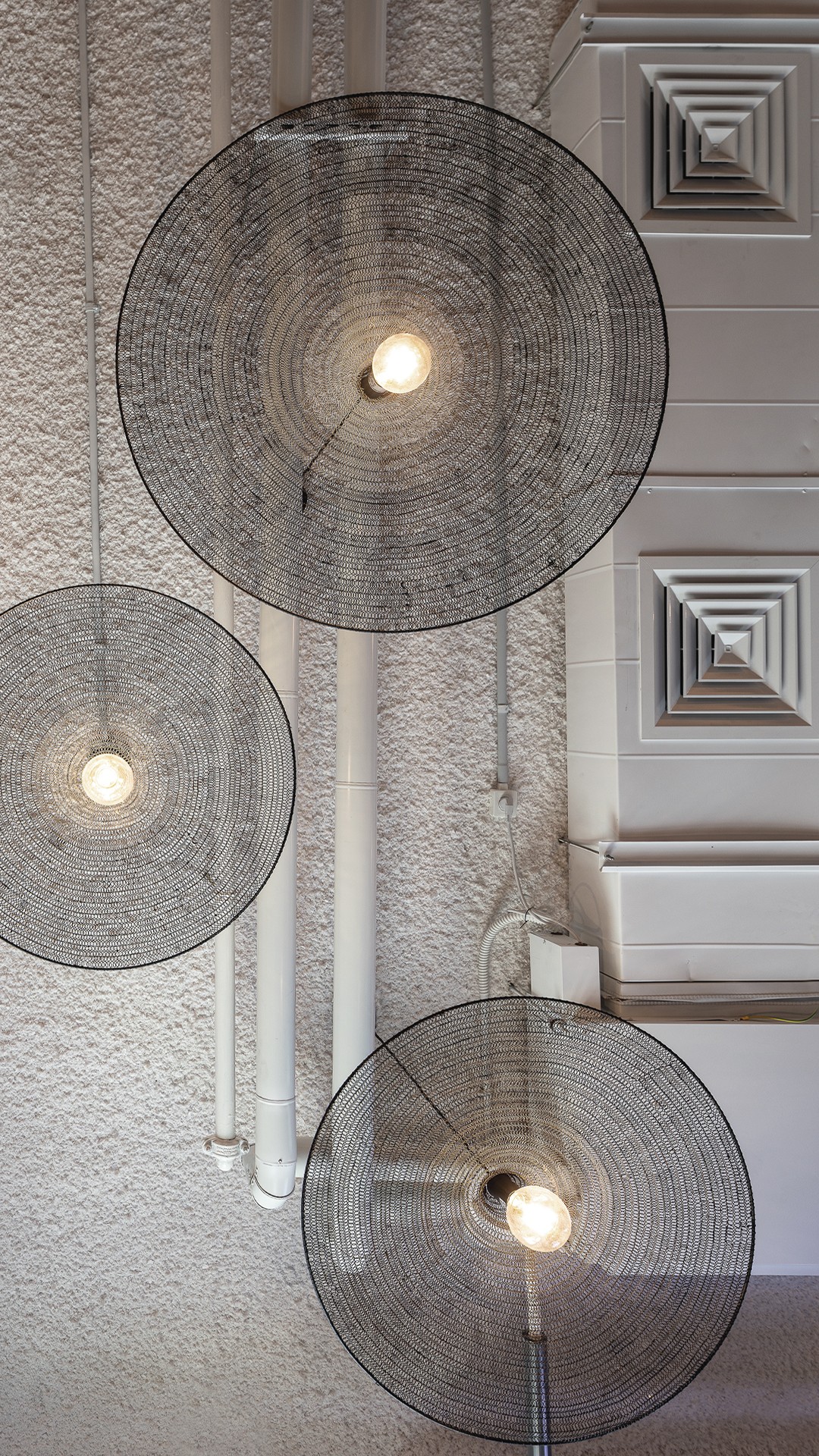 תאורה ואווירה: תקריב על גופי התאורה הדקורטיביים מרשת שחורה (Wire Mesh Pendants), המשתלשלים מהתקרה ומוסיפים חמימות וטקסטורה תעשייתית לחלל הקפיטריה.