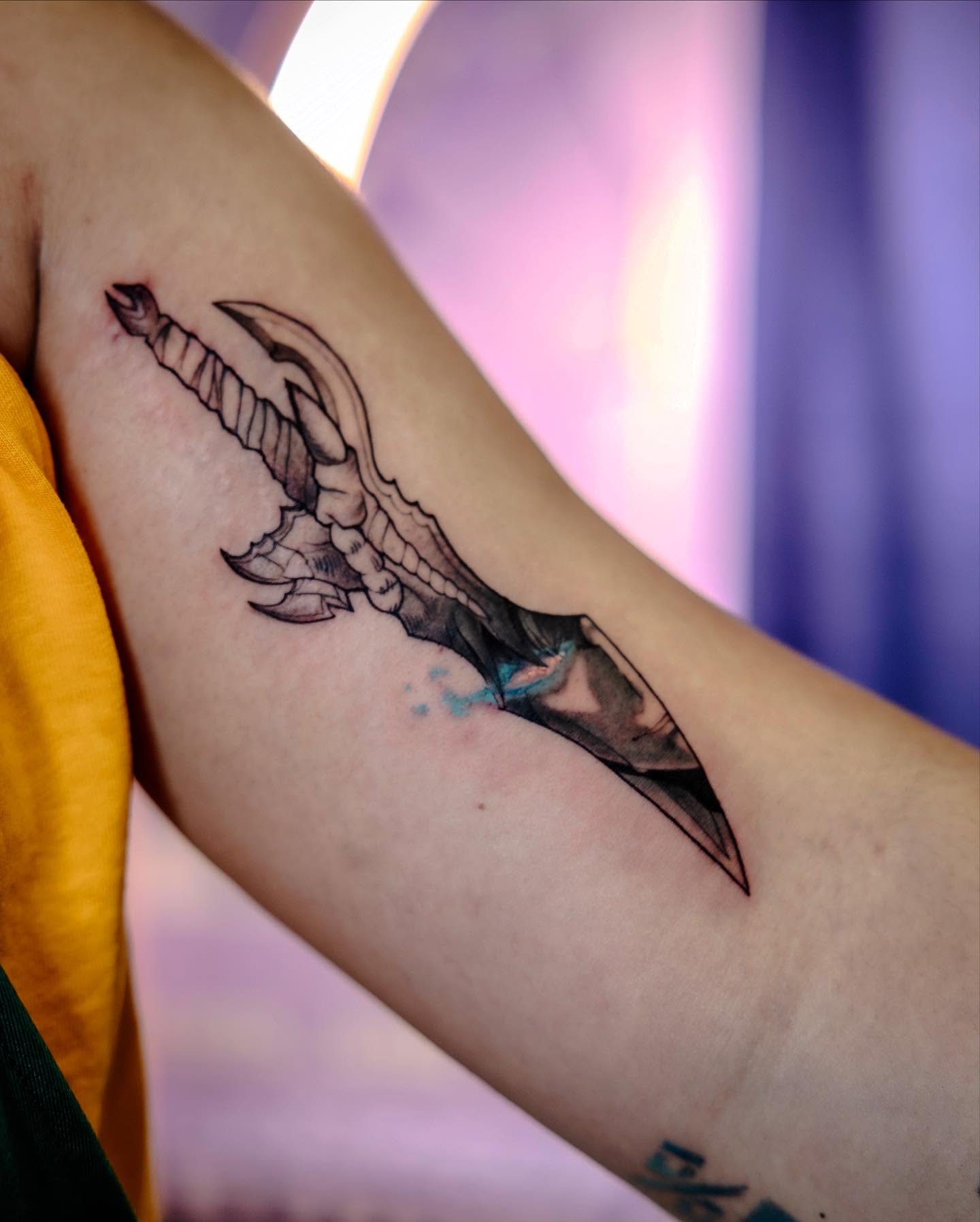 A grayscale anime-style tattoo of a character with spiky hair and a headband, holding a kunai.  The tattoo is on someone's forearm.