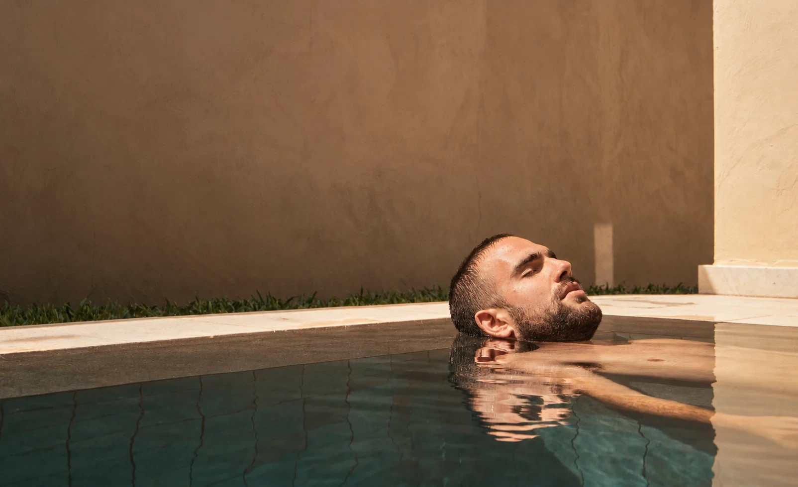 Hombre relajándose en el agua con la cabeza apoyada en el borde de la piscina