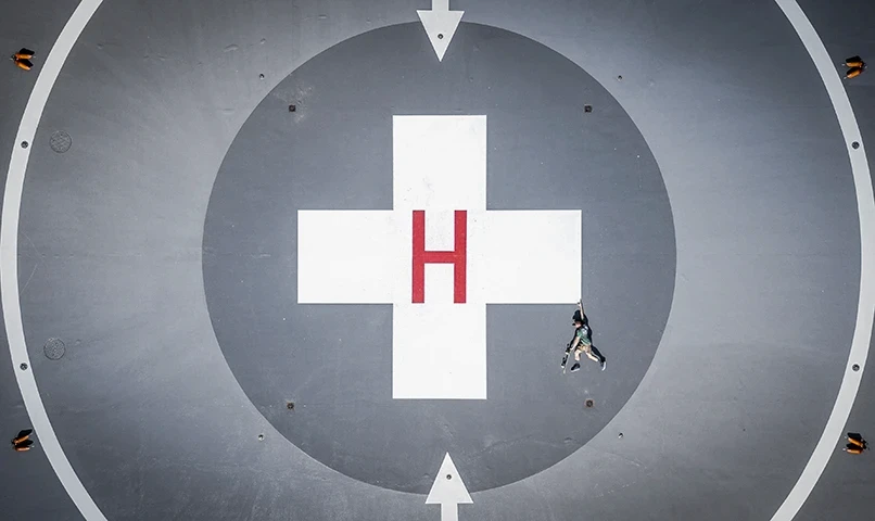 Widok z lotu ptaka na lądowisko dla helikopterów z literą H i osobą leżącą pośrodku w centrum symetrycznego wzoru