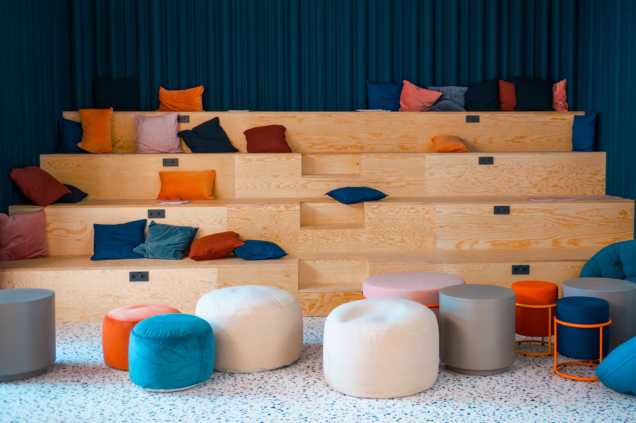A modern interior featuring wooden shelves filled with colorful items and various poufs on the floor.
