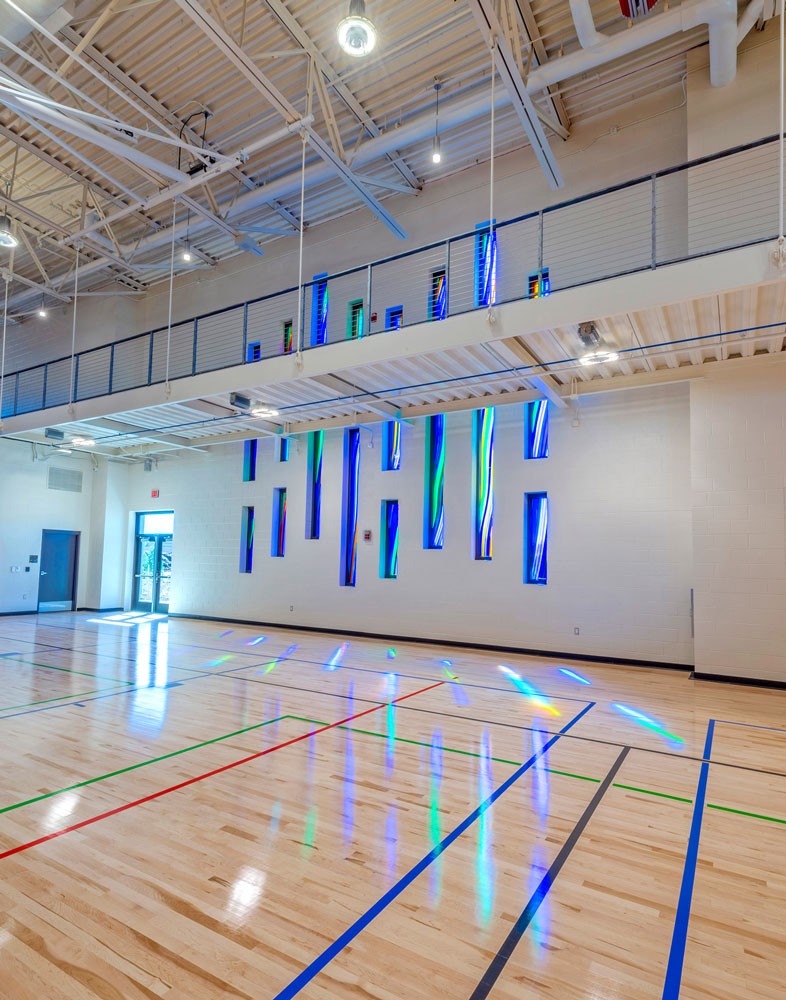 Vertical architectural glass installations casting colored light across gym floor, reflecting movement and activity in public recreation space