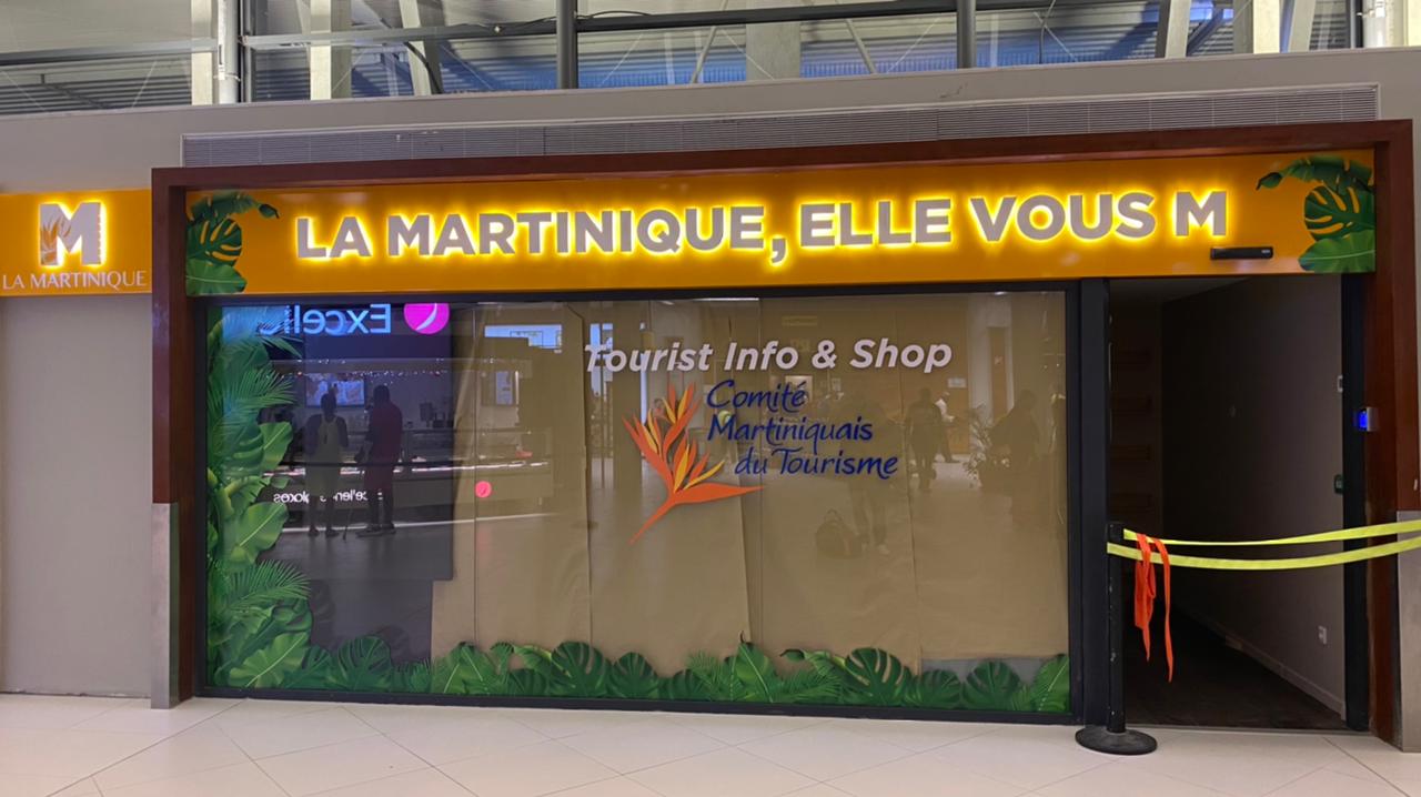 Une boutique nommée « La Martinique, Elle Vous M » avec une décoration tropicale et une enseigne lumineuse. La boutique propose des informations touristiques et est située dans un quartier animé.