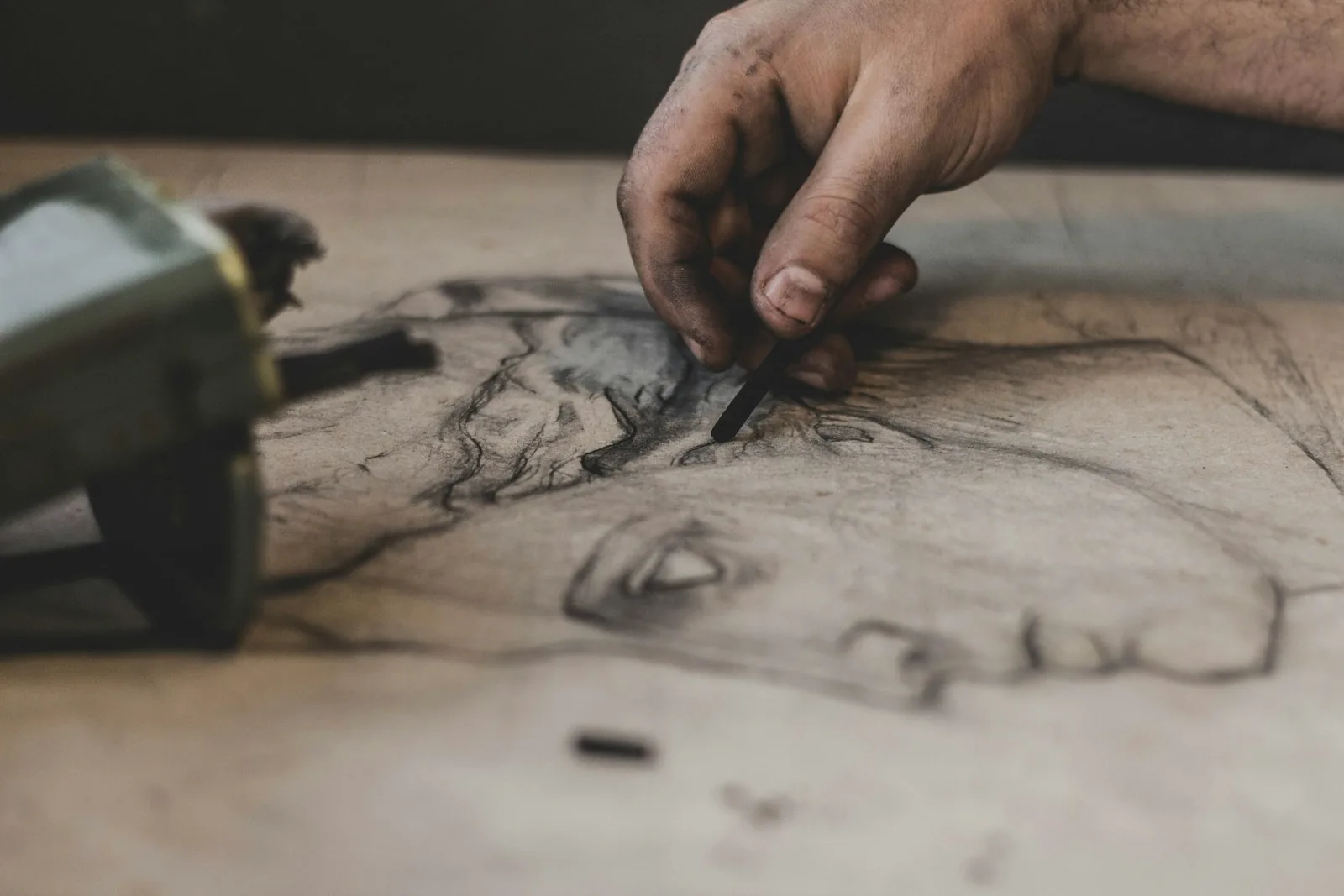 Charcoal-smudged hand drawing a large rough portrait sketch with a charcoal stick on beige paper