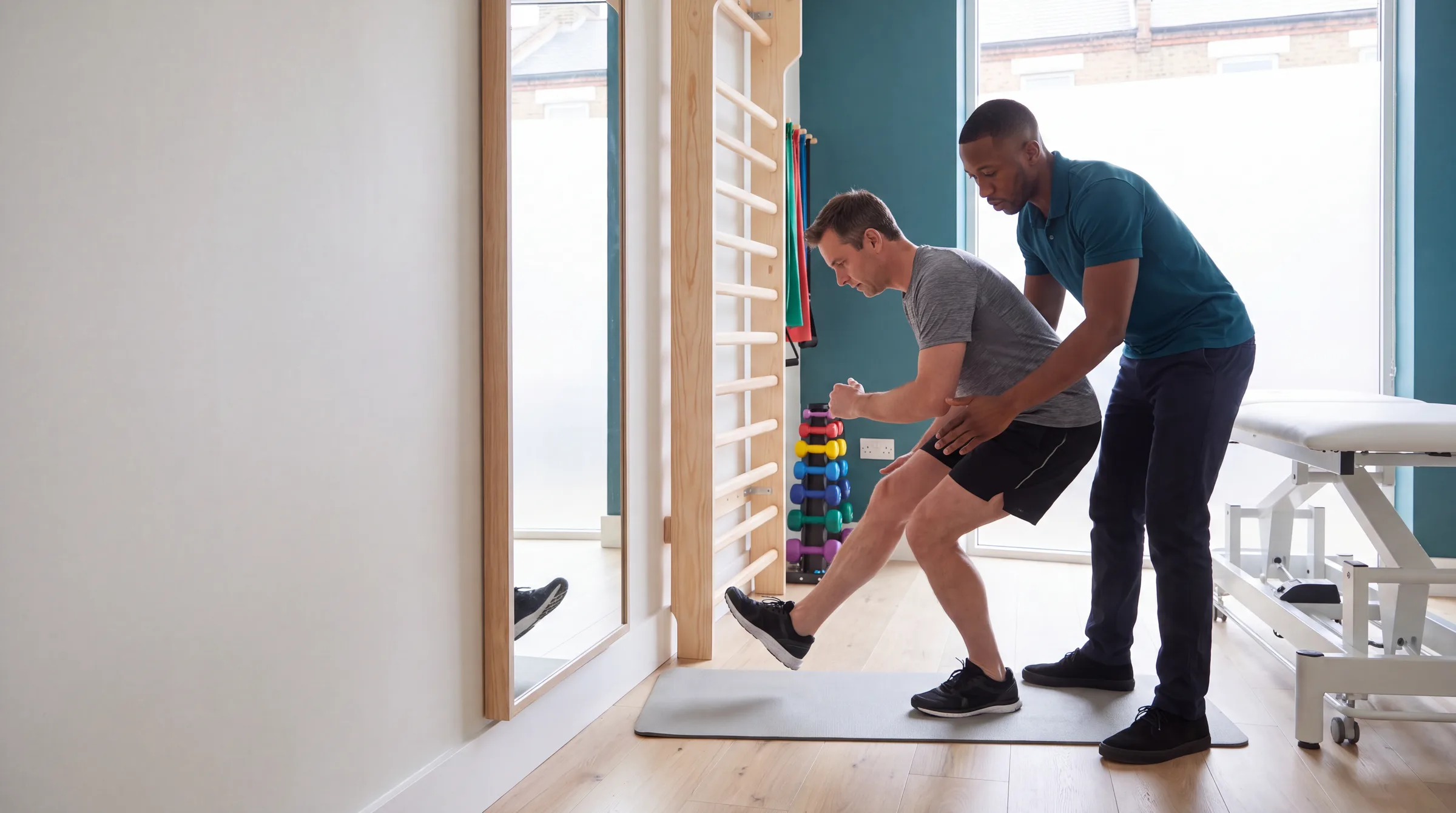 A physiotherapist guiding a runner through a single-leg squat beside the wall bars