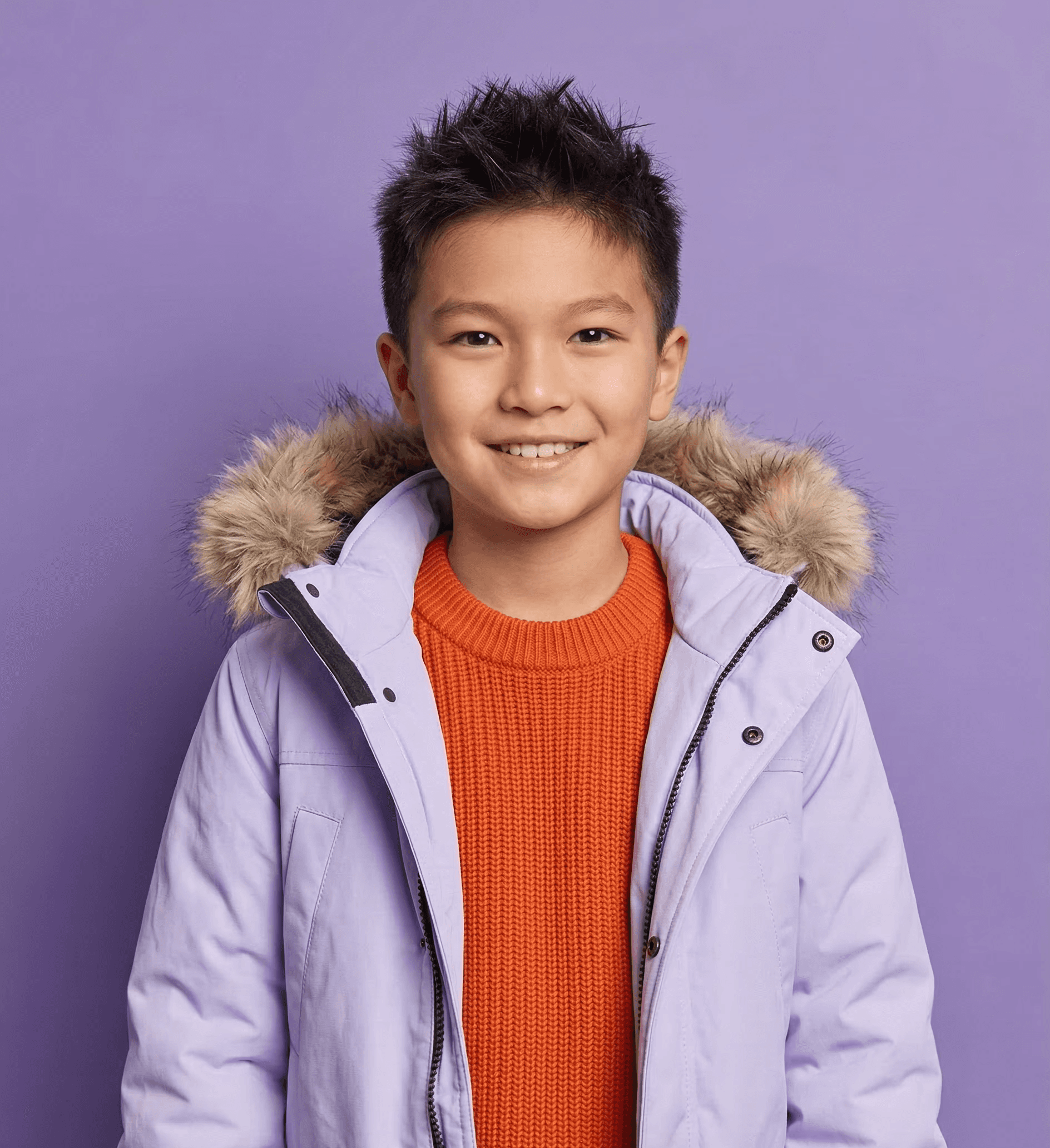 A smiling child in orange fisherman sweater and light purple parka