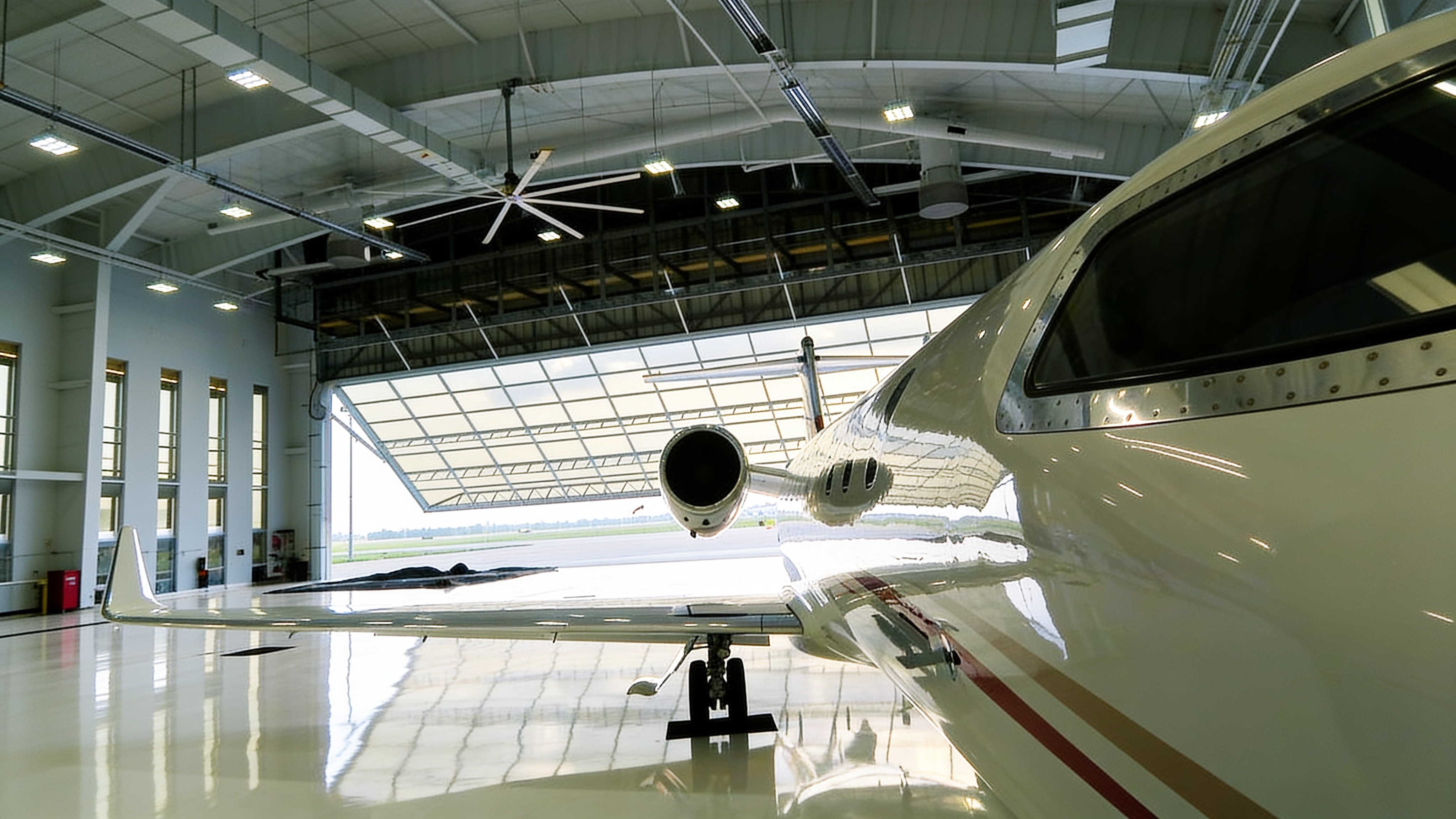 Private jet inside a hangar with a raised glass hydraulic door