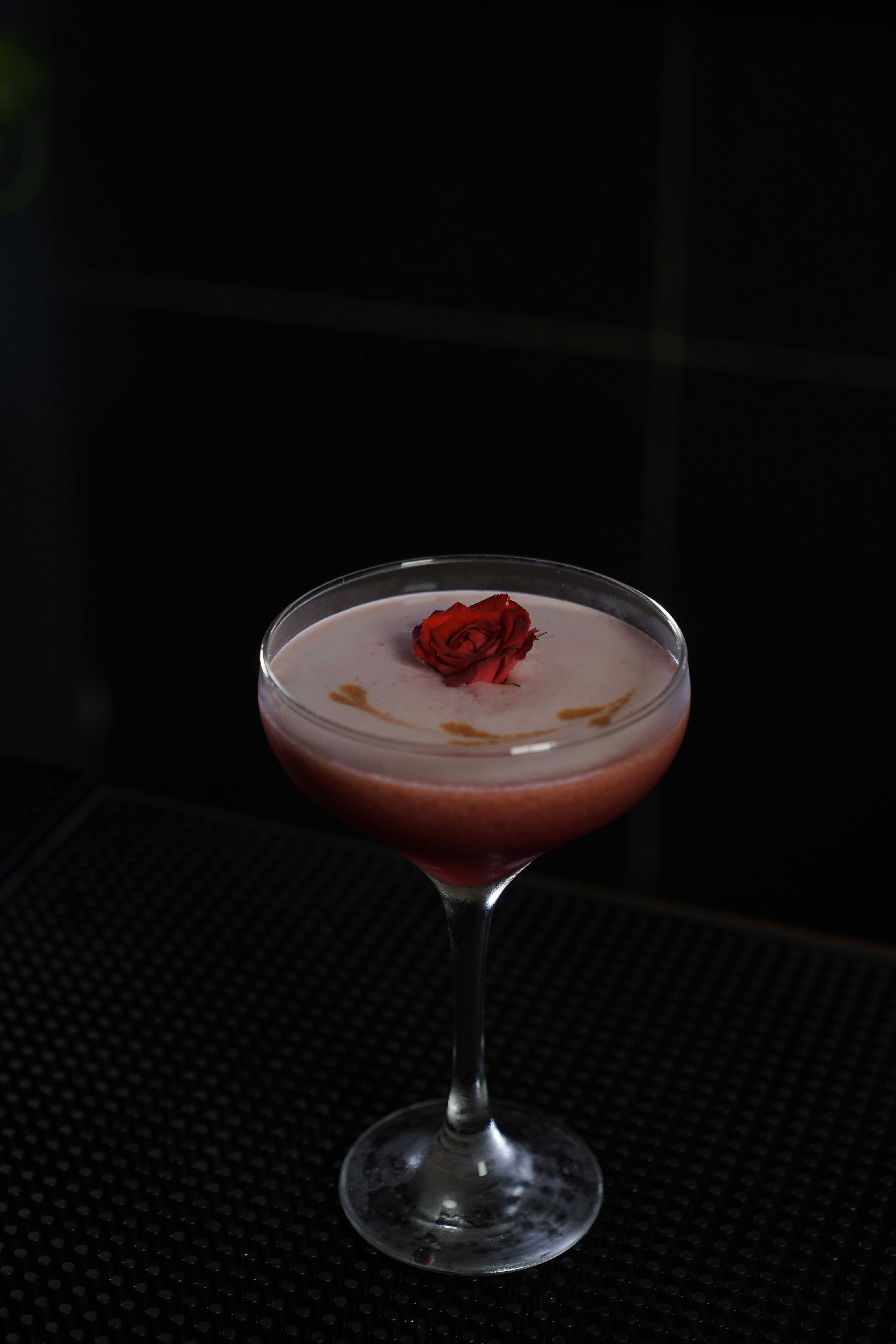 A pink cocktail garnished with a red flower