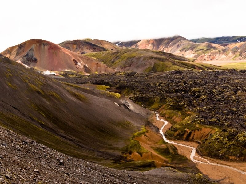 View over Landmannalaugar in Iceland showing multicolored rhyolite mountains, the dark Laugahraun lava field, and the winding Graenagil ravine from Bláhnjúkur in Fjallabak Nature Reserve.
