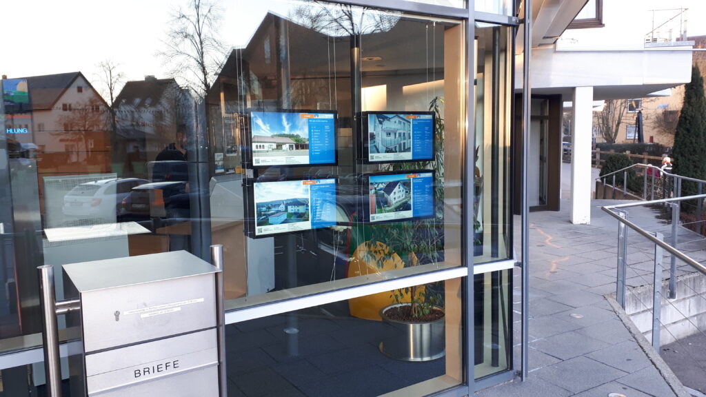 Real estate listings on four digital screens in a window display.