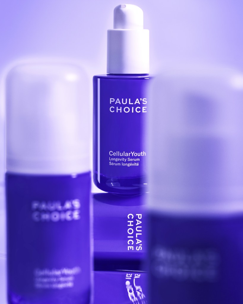 A display of skincare products from Paula's Choice, featuring a purple bottle of CellularYouth Longevity Serum in the foreground and additional purple bottles slightly blurred in the background.