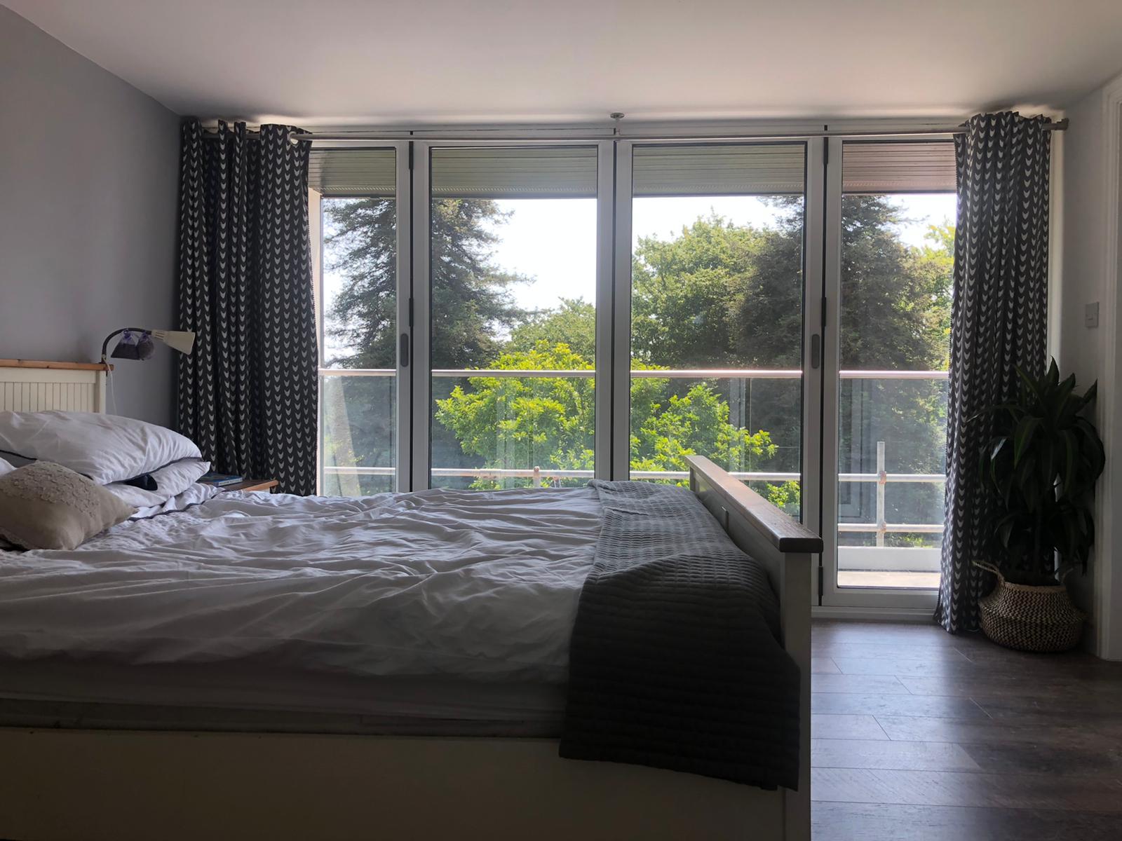 Modern glass and wood cabin with a cozy outdoor deck featuring wicker furniture, surrounded by lush green trees and a serene forest setting.