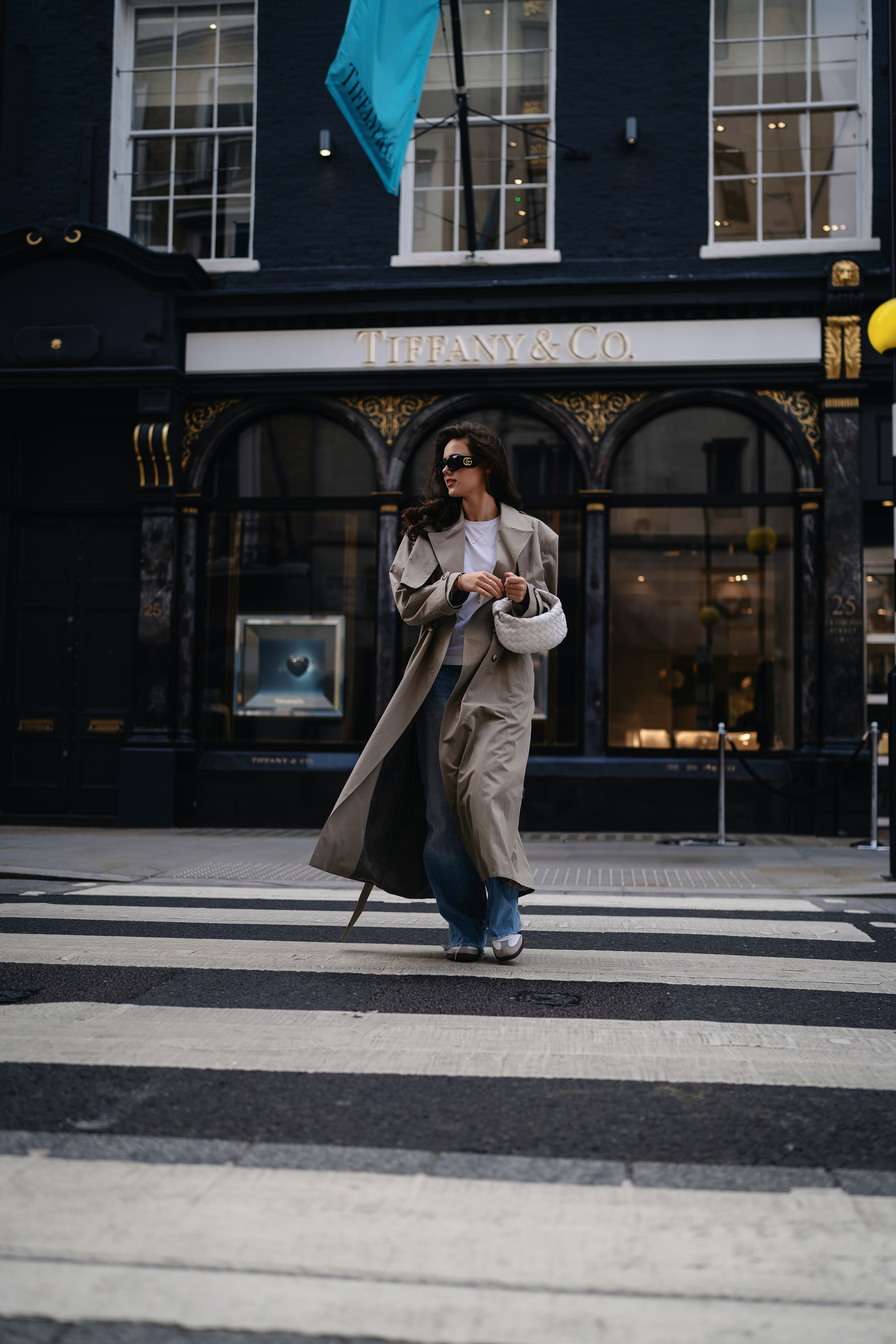 A woman walking across a street holding a blue umbrella