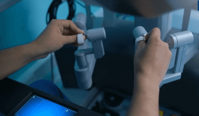 Close-up of Dr. Tushar’s hands operating the precise joystick controllers of the da Vinci surgical robot.