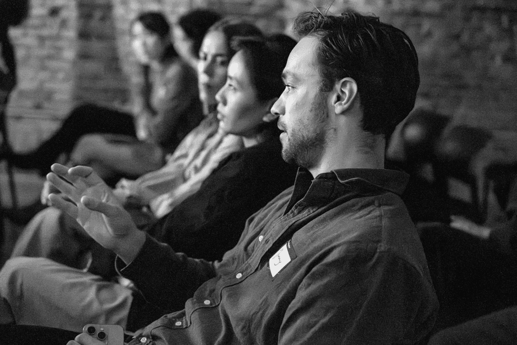 Black and white image of people working at a table with laptops, showing hands gesturing during discussion of digital content displayed on screens, with fabrica® logo in the corner.