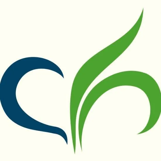 A young woman with long brown hair smiles warmly against a green background, dressed in a black jacket and white shirt.