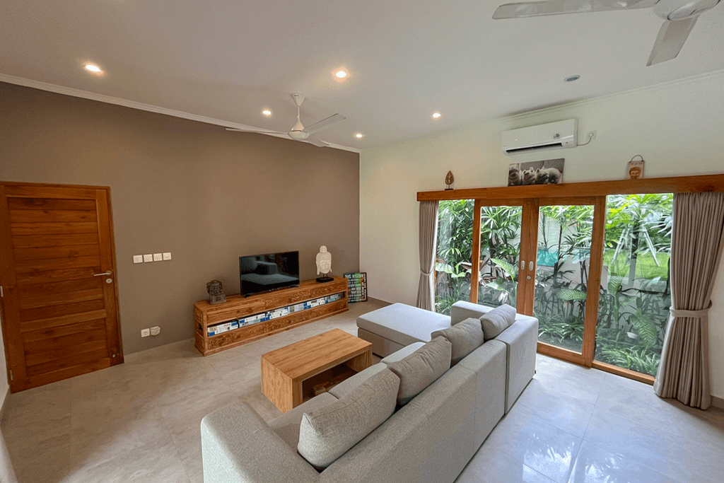 Minimalist living room with garden views through glass doors. Expert real estate services for Canggu properties.