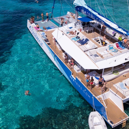 Катамаран під назвою "Seacat", на якому люди засмагають, плавають та відпочивають на палубі в яскравих бірюзових водах.