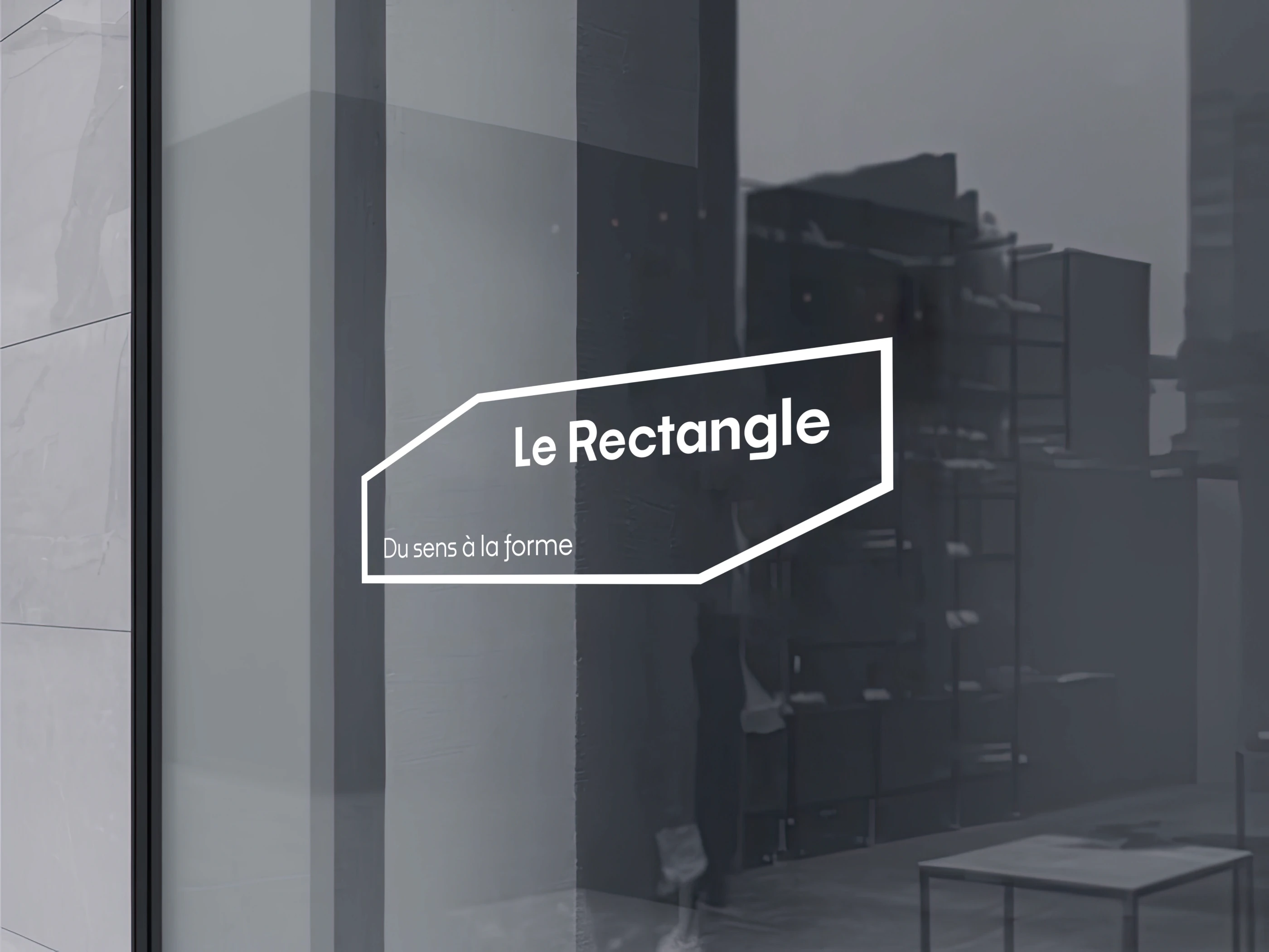 Logo Le Rectangle appliqué en vitrophanie blanche sur la vitrine sombre des locaux de l'agence.