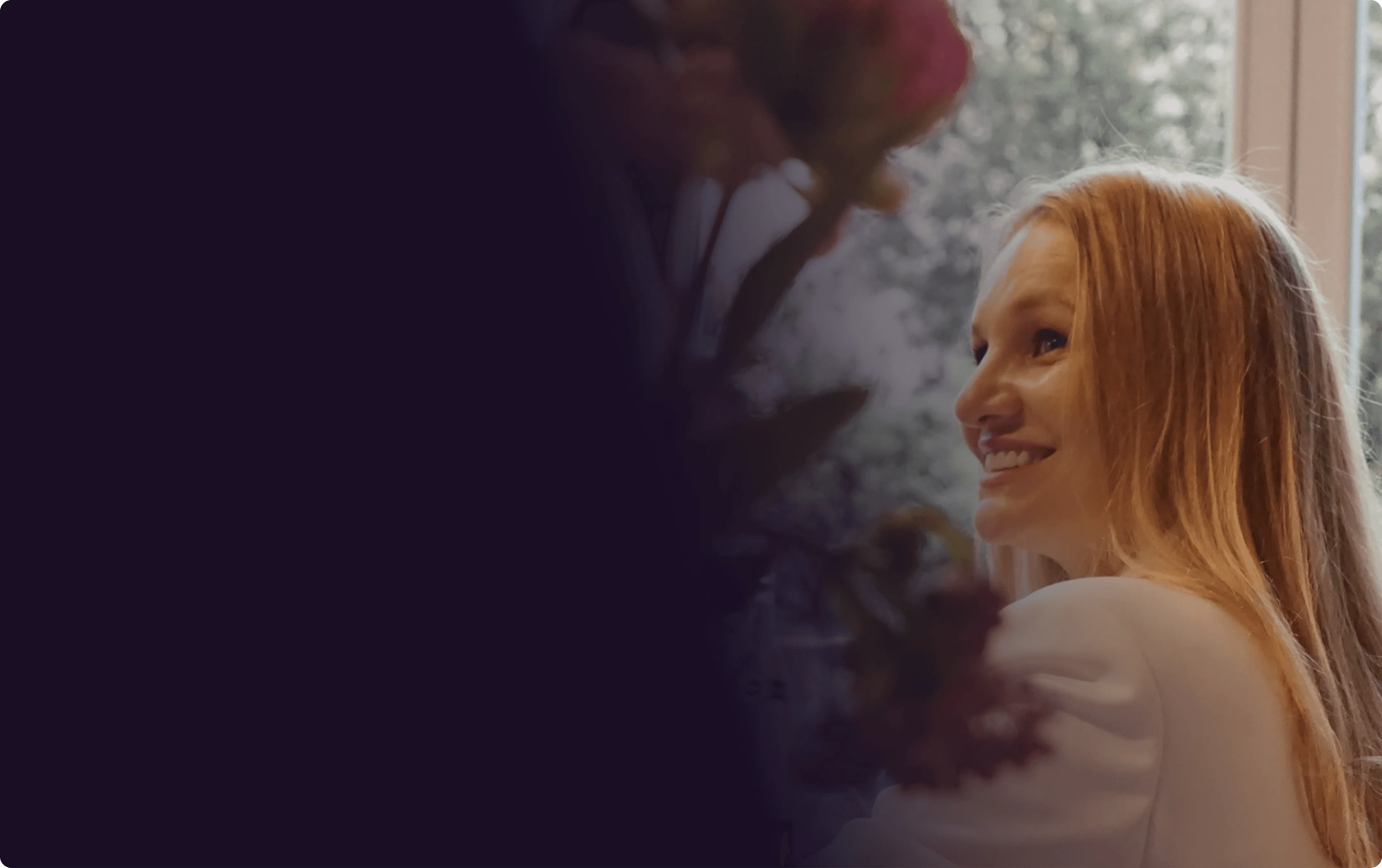 A woman with long, light hair smiles gently, surrounded by soft lighting and floral elements in the background.