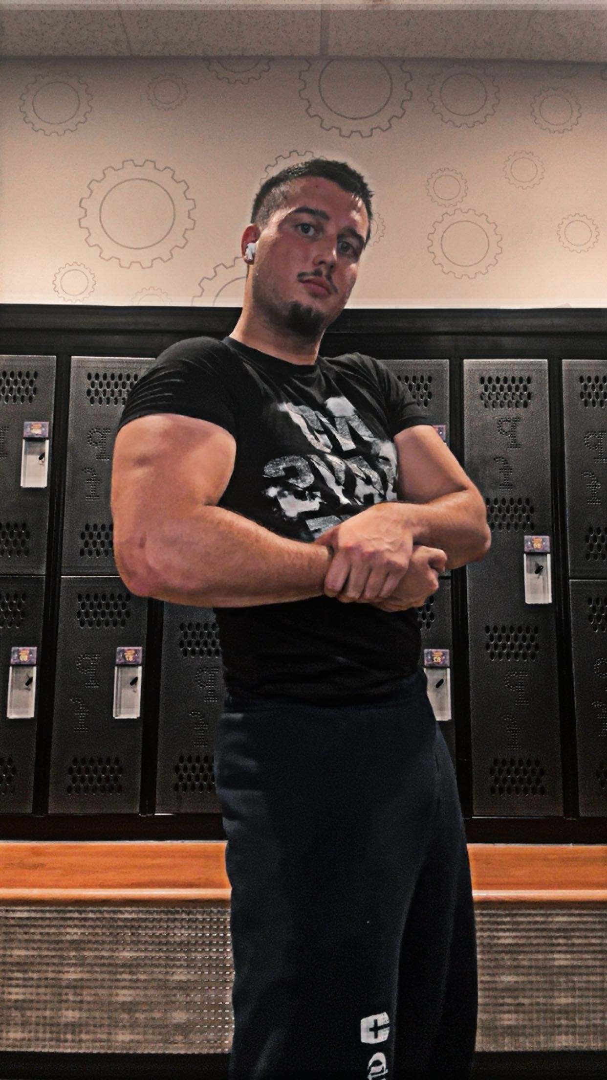 A person in a gym locker room flexing his bicep at the camera