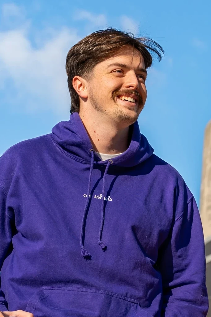 Émile SEGURET, cofondateur de On Wheels, souriant en portant un hoodie violet sous un ciel bleu