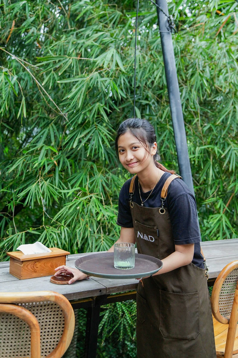Smiling resort team member standing in front of lush tropical greenery.