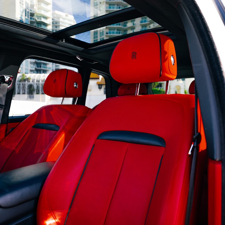 Luxurious rear seating of white Rolls-Royce Cullinan, spacious red interior for chauffeur service Miami.