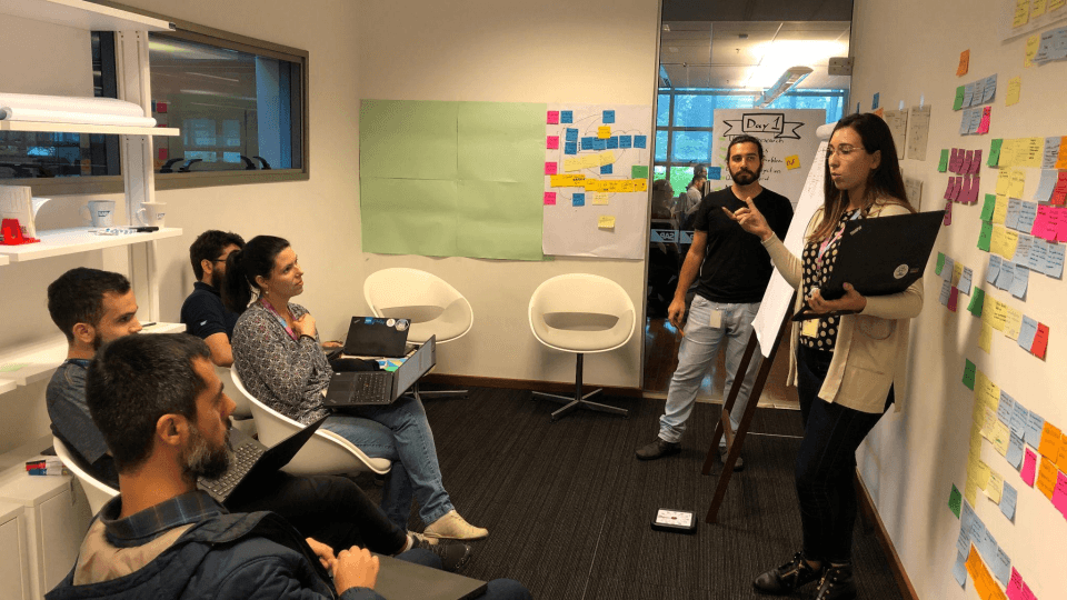 The project team discussing research findings in a design sprint room lined with sticky notes