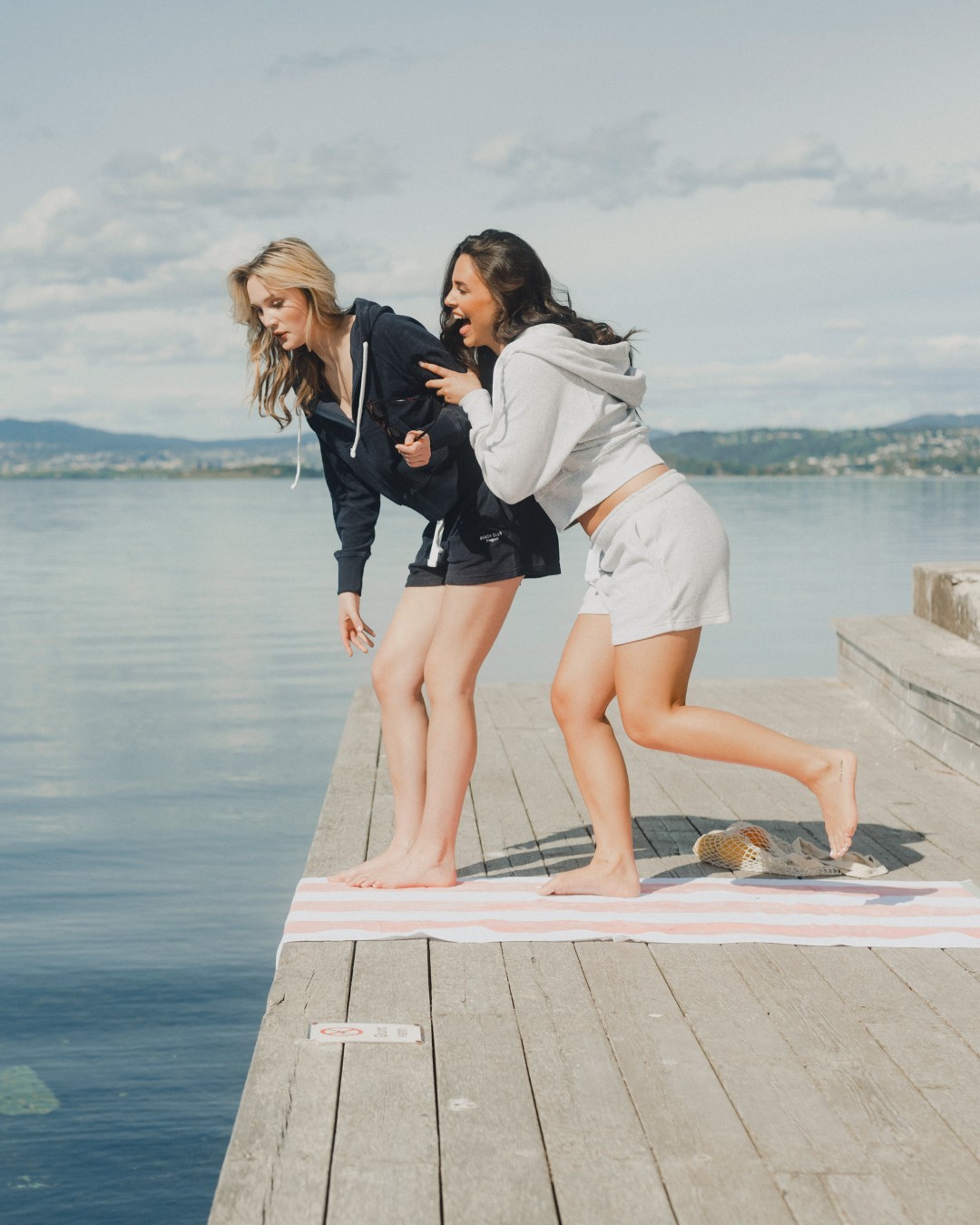 Two women by the water wearing navy and light grey hoodies with matching lounge shorts, relaxed casual summer outfits.