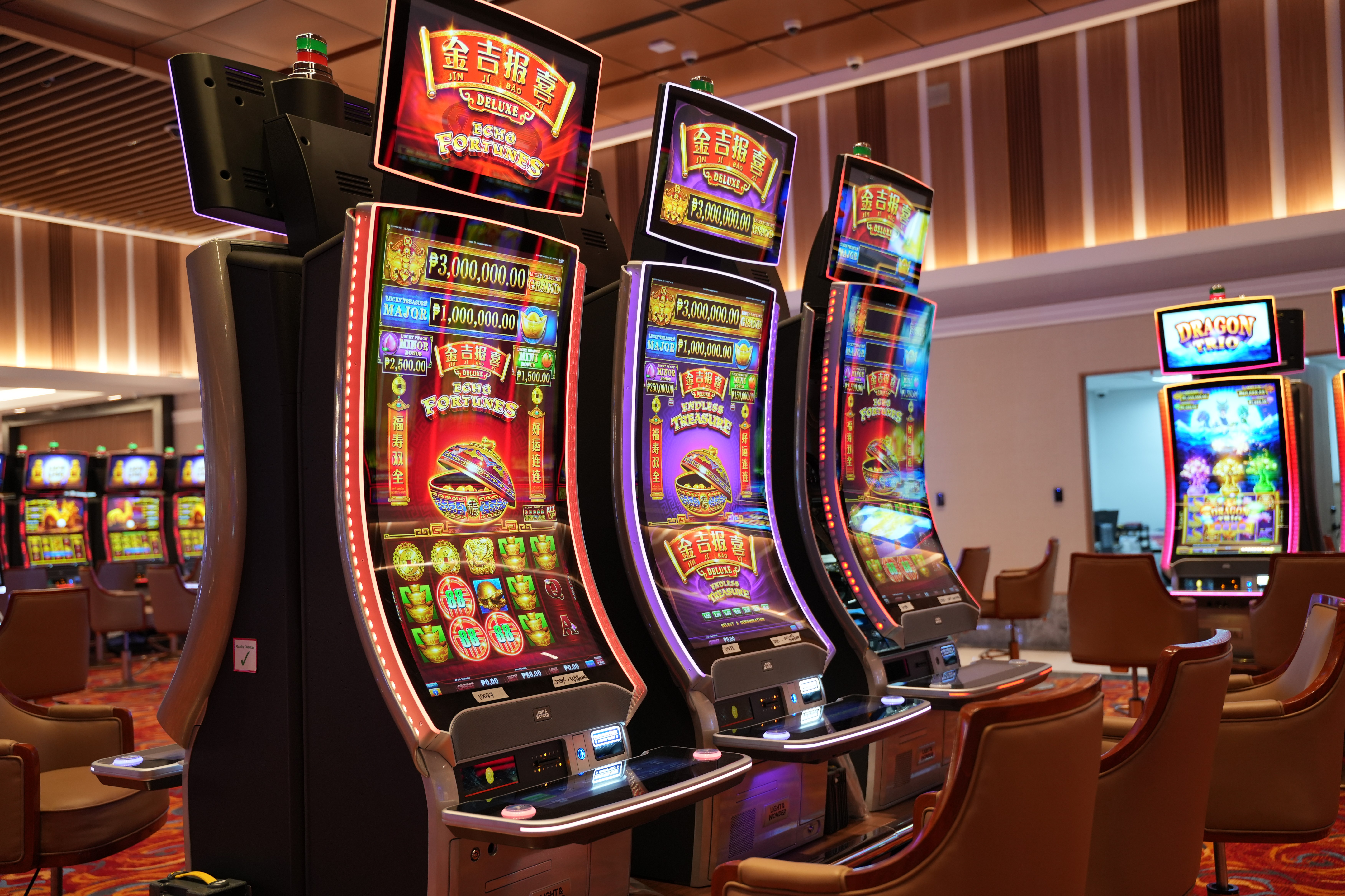 Three stylish Asian friends taking a selfie together inside a glamorous casino, bright slot machines in the background, warm lighting, energetic smiles, atmosphere full of excitement — editorial photography style.