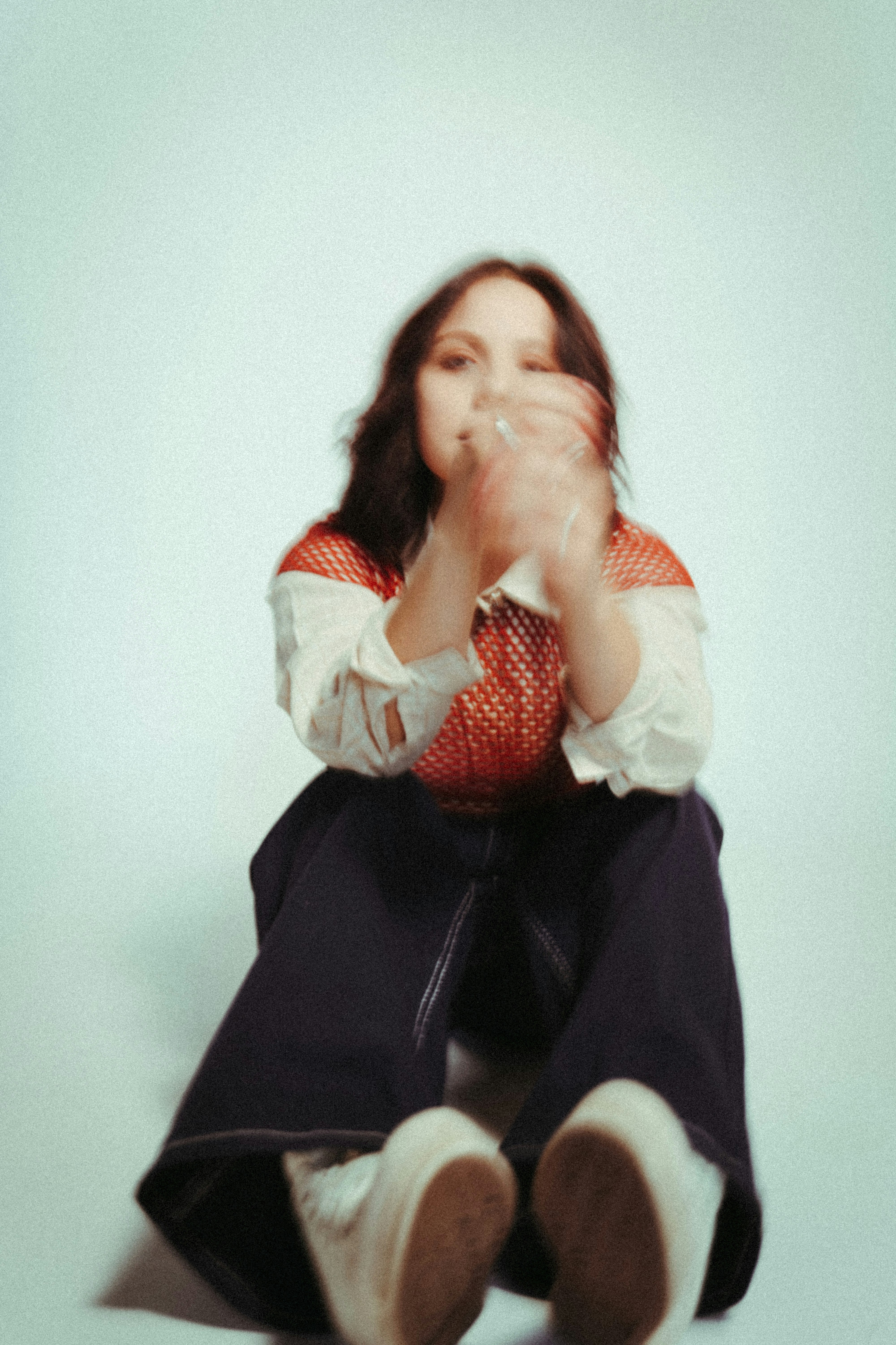 Seated portrait of a person with long hair, wearing casual clothing and looking toward the camera, slightly blurred for a soft artistic effect.