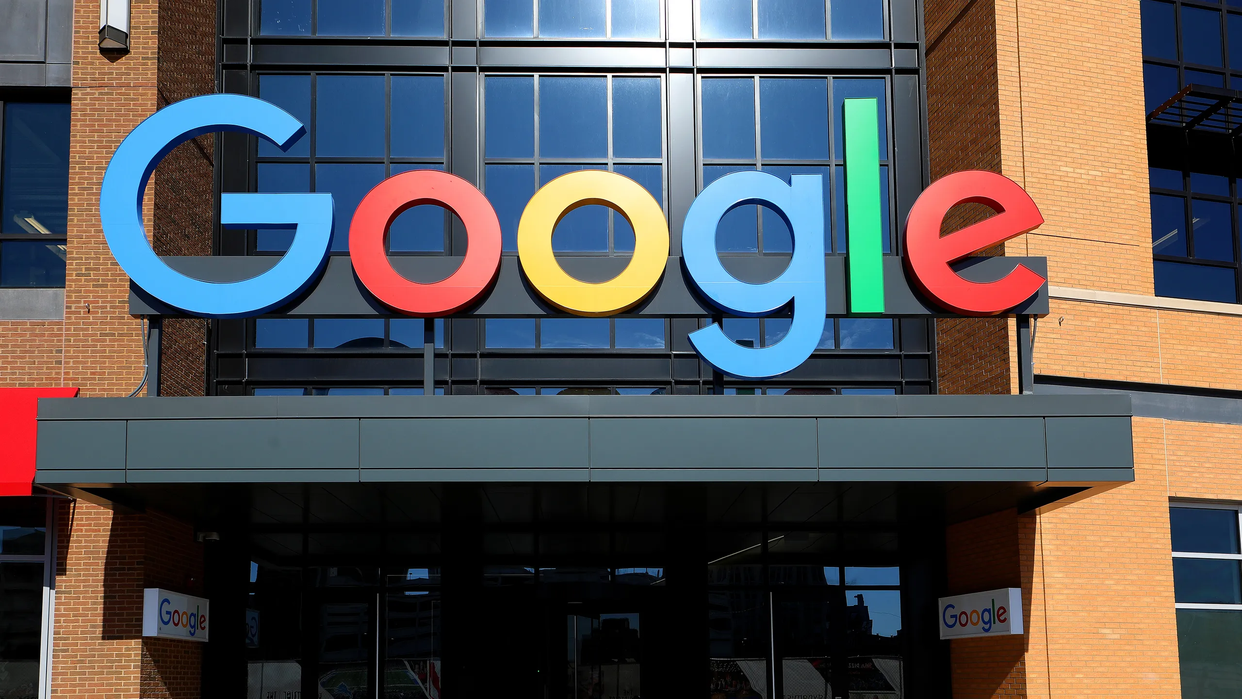 Google logo in colorful letters mounted on the exterior of a modern office building with glass windows and a brick facade.