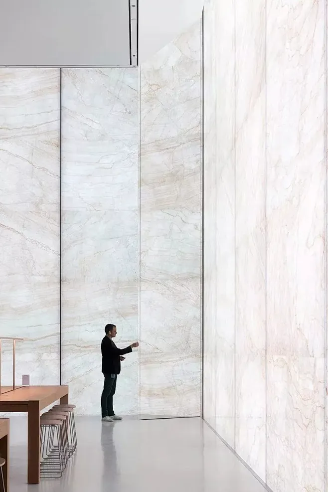 A man observing large white marble slabs with subtle natural veining in a spacious interior setting.