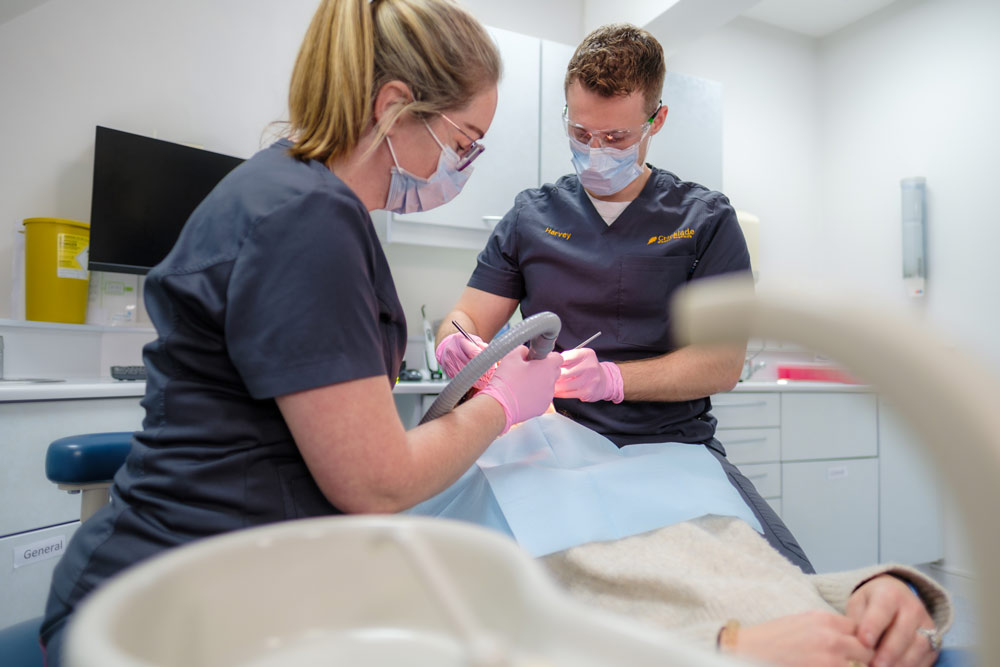 Two dental professionals wearing protective masks and gloves consult over dental equipment in a modern clinic.