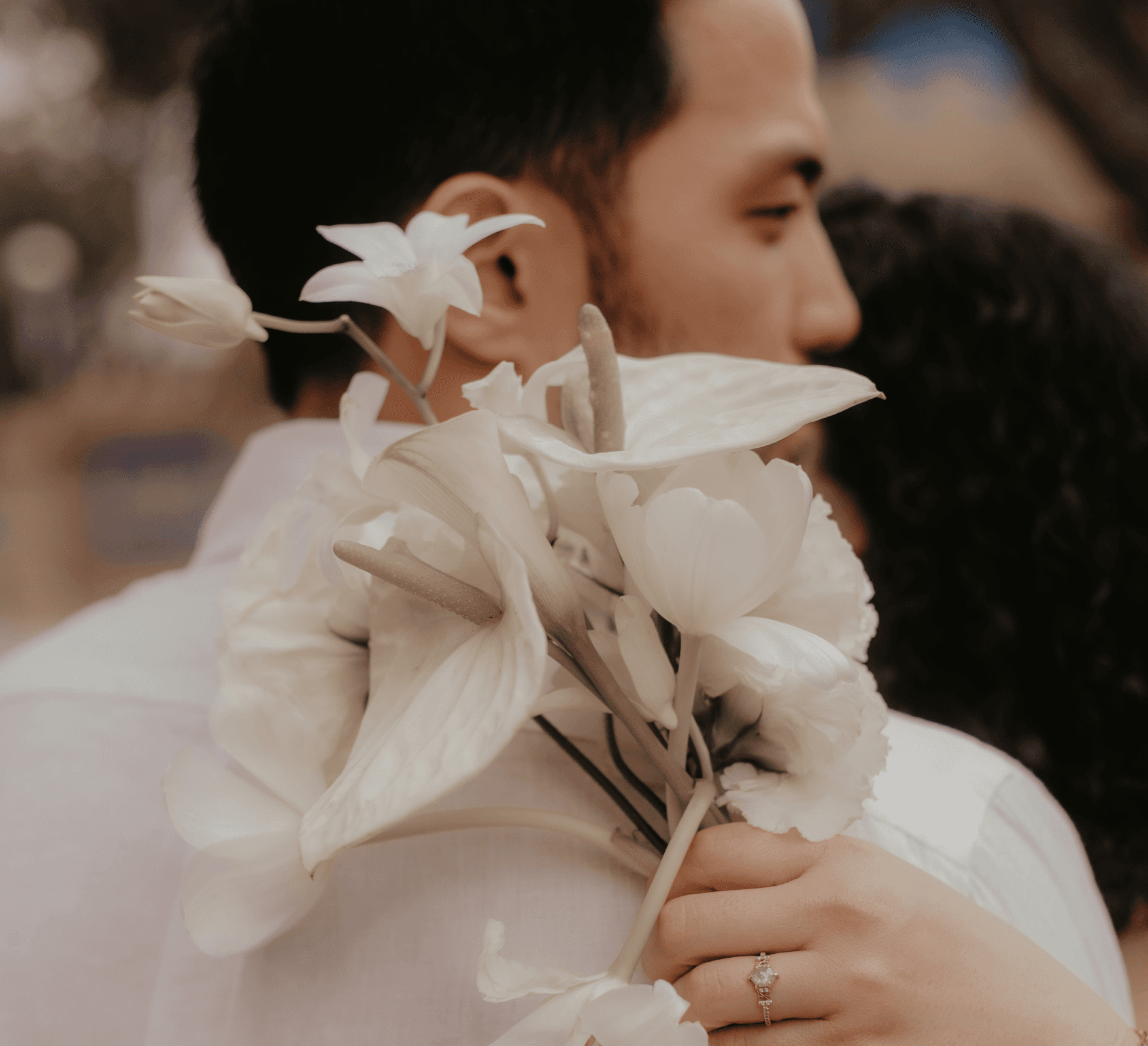 Close-up of two hands gently clasped, one wearing a sparkling engagement ring. The soft lighting and pastel nails evoke a sense of romance and intimacy.
