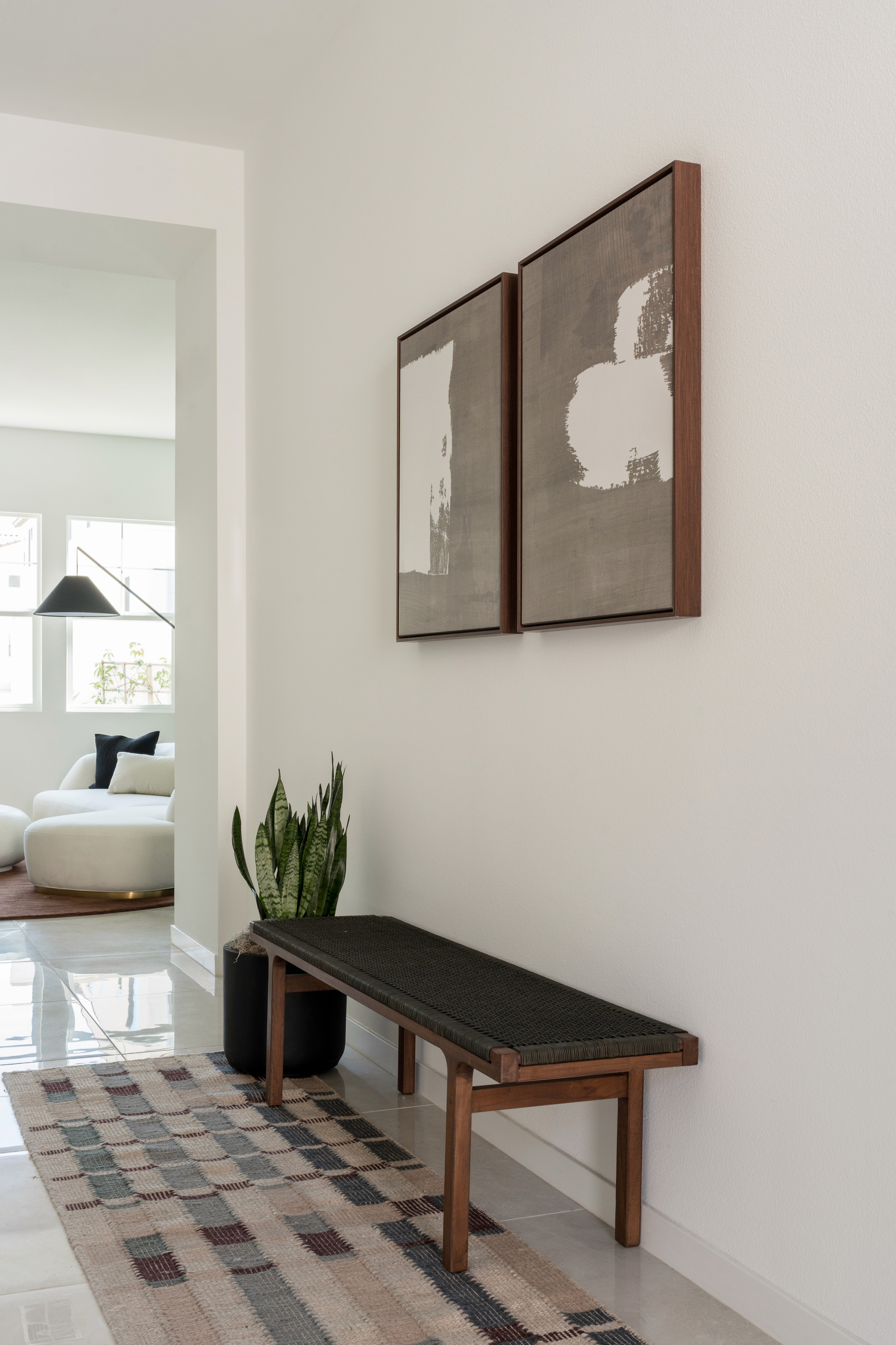 Entryway with warm wood and black rope bench, wood framed modern artwork, neutral multi-colored runner, and potted greenery by Jubilee Interiors in Arcadia, California