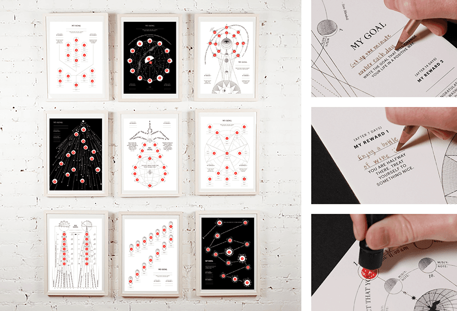 A grid of nine framed prints on a white brick wall displays various diagrams and charts. Each print includes black-and-white line drawings and text labels such as “MY GOAL,” “Get my reward,” and “My reward 1.” A hand holds a pen, pointing to a small red dot on one of the prints. The background is a white brick wall with visible mortar lines.