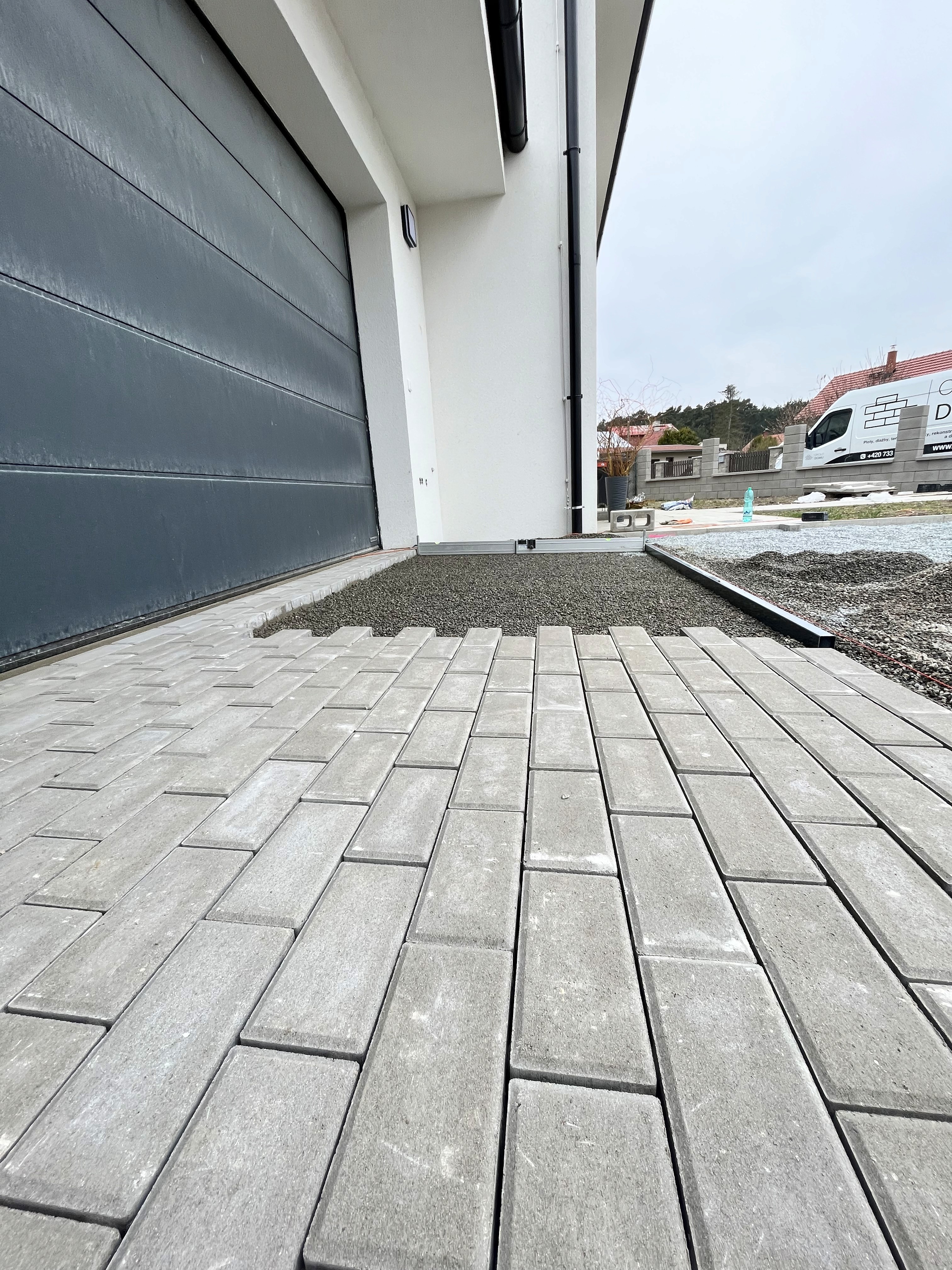 Nová šedá zděná zeď s pilíři a chodník z dlažebních kostek. Stavební práce, dům v pozadí.