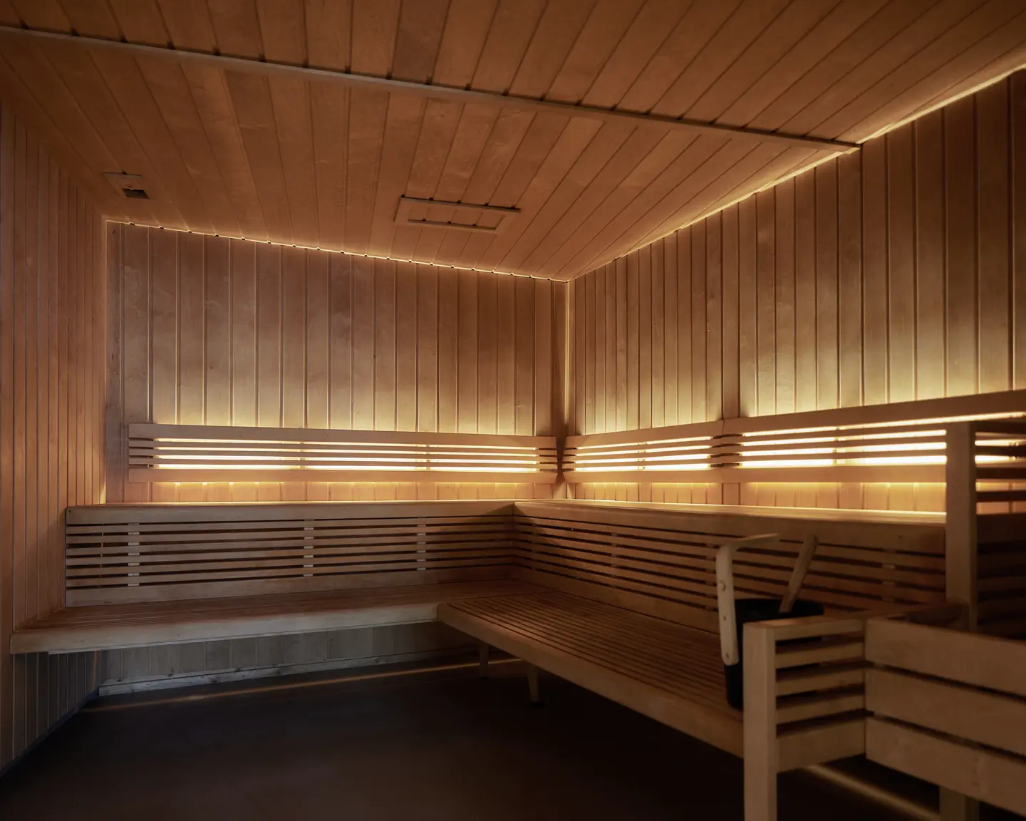 Warmly lit wooden sauna interior with tiered slatted benches and wood-paneled walls.