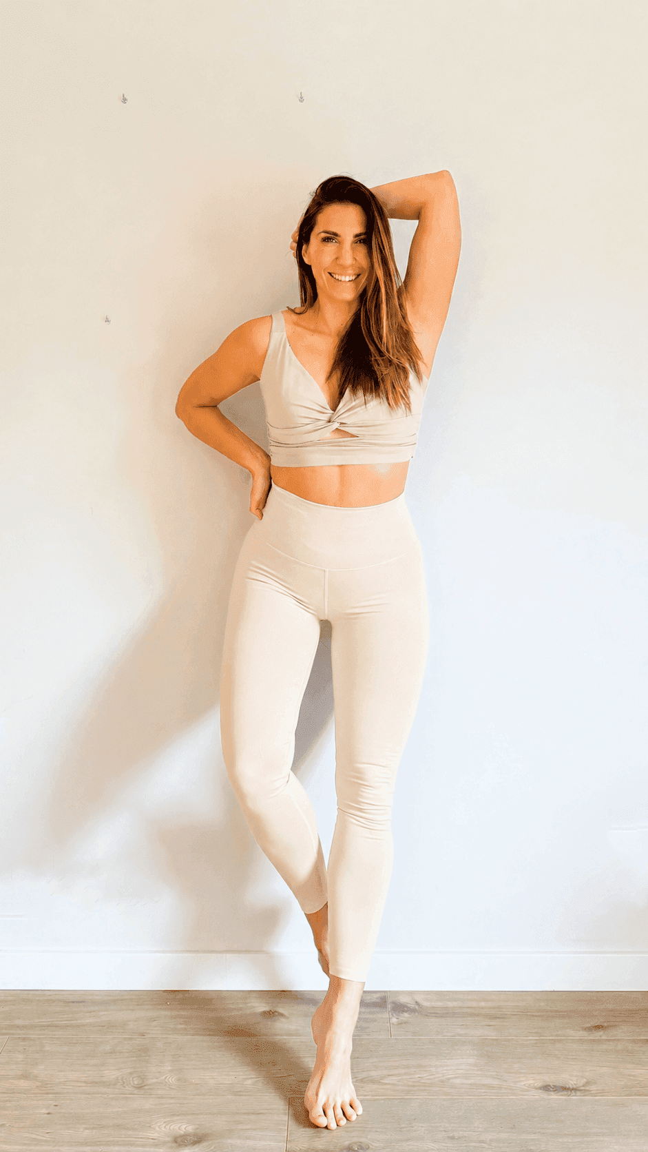Photo de Caroline, fondatrice de l'application FitMum France, effectuant un étirement latéral doux (posture du guerrier) sur un parquet. Elle incarne la coach sportive spécialisée grossesse et post-partum, attentive et bienveillante. Idéal pour introduire la section d'aide personnalisée de la page Contact.