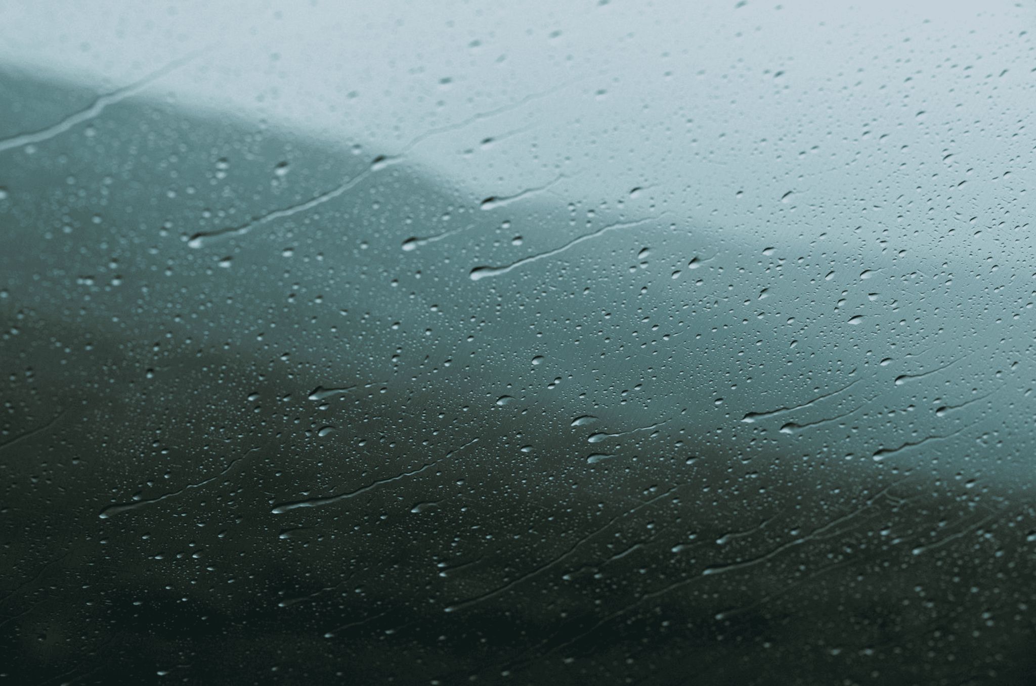 Close-up of raindrops streaking down a window, with a hazy landscape blurred behind