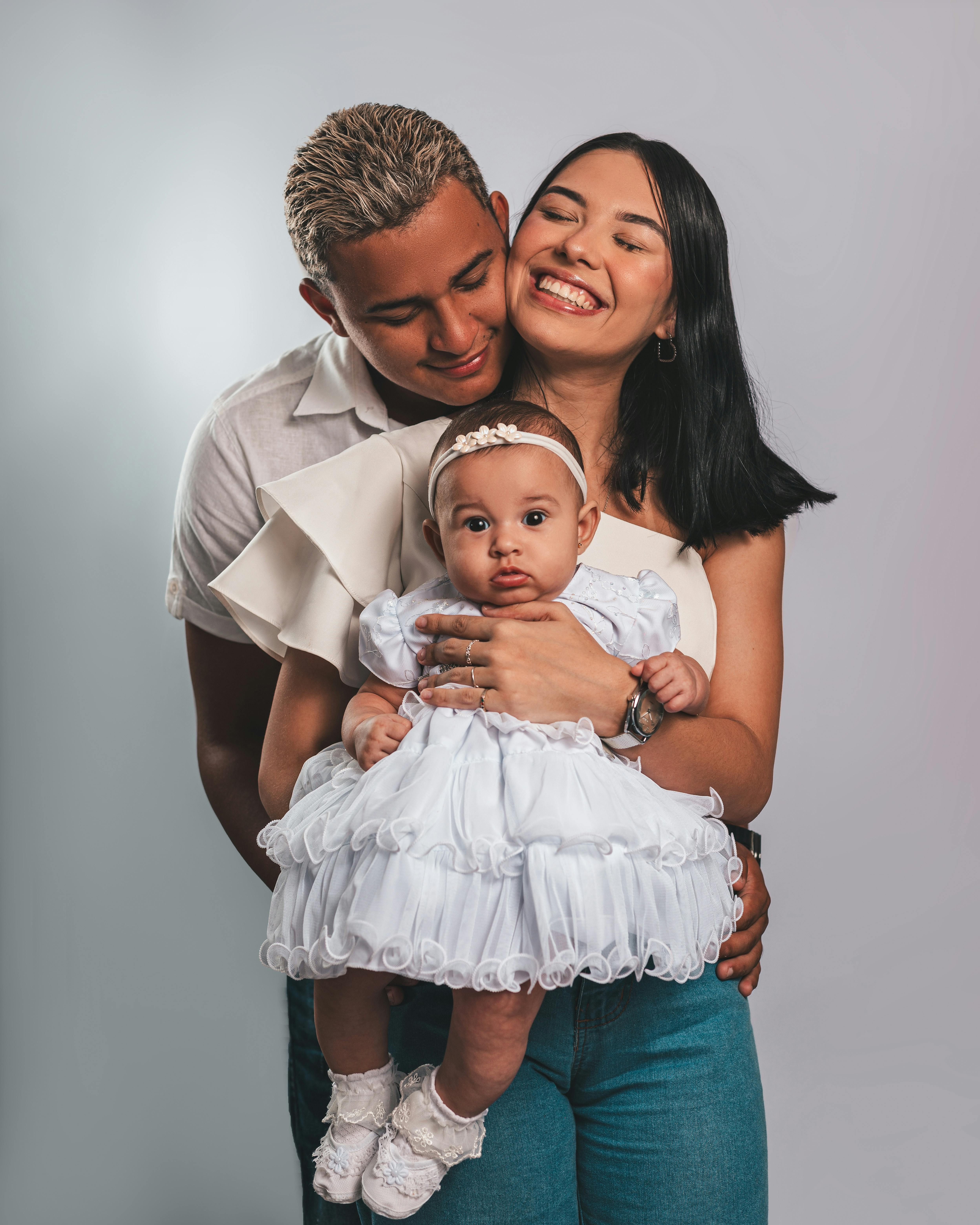 Une famille souriante composée d'un homme, d'une femme et d'un bébé, se tenant rapprochés pour une photo de famille.