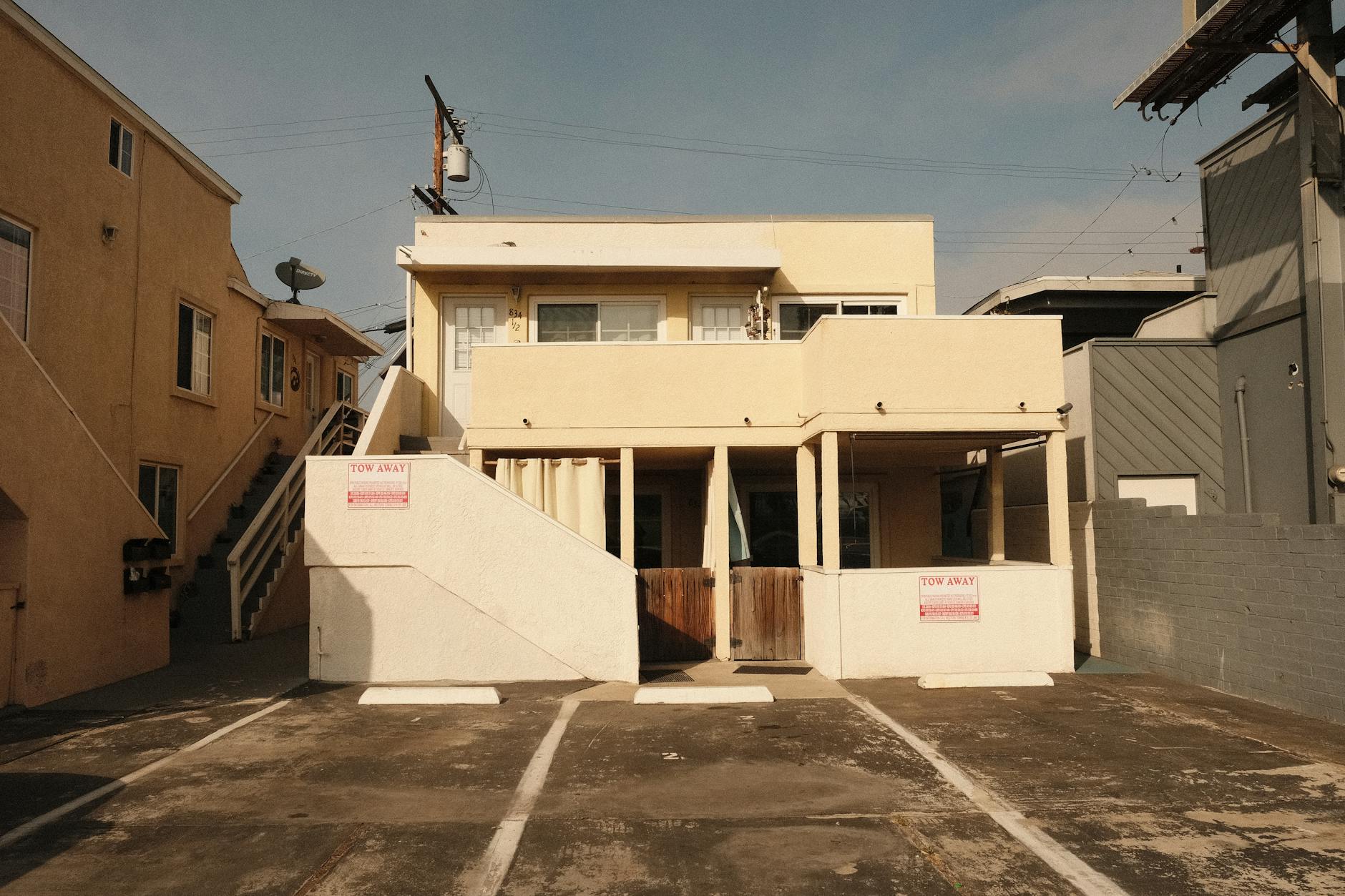 Two-storey cream-painted rental block with an external staircase and For Rent signs on the ground floor units