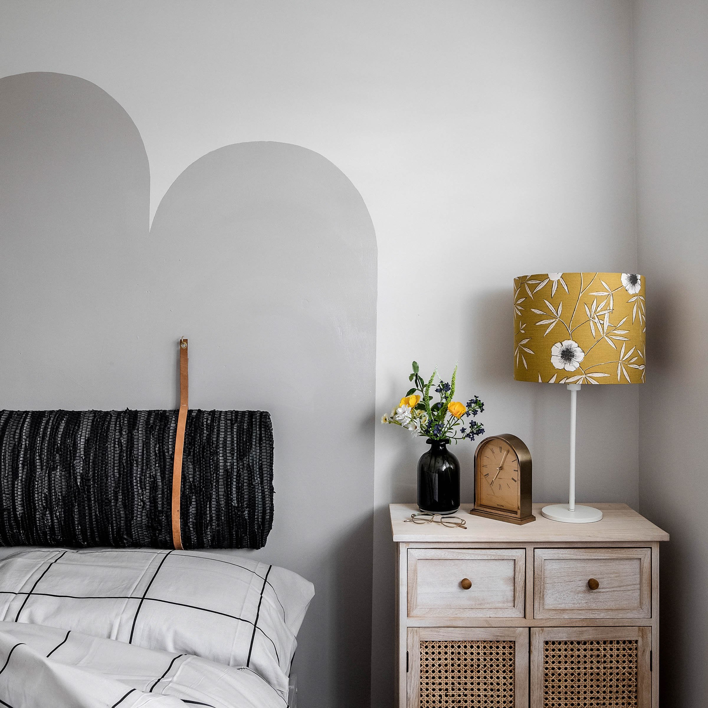 Close-up of bedroom bed with arched painted headboard, cushion attached to the wall,, bedside table, clock and lamp, Atelier Akuko