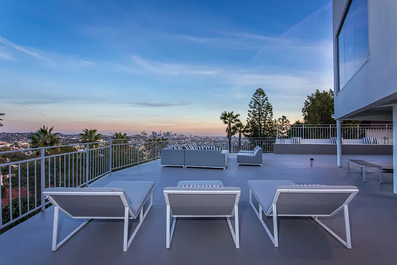 A modern white SUV is parked in a stylish driveway under a sleek carport. A woman in business attire walks towards the vehicle, conveying a professional tone.