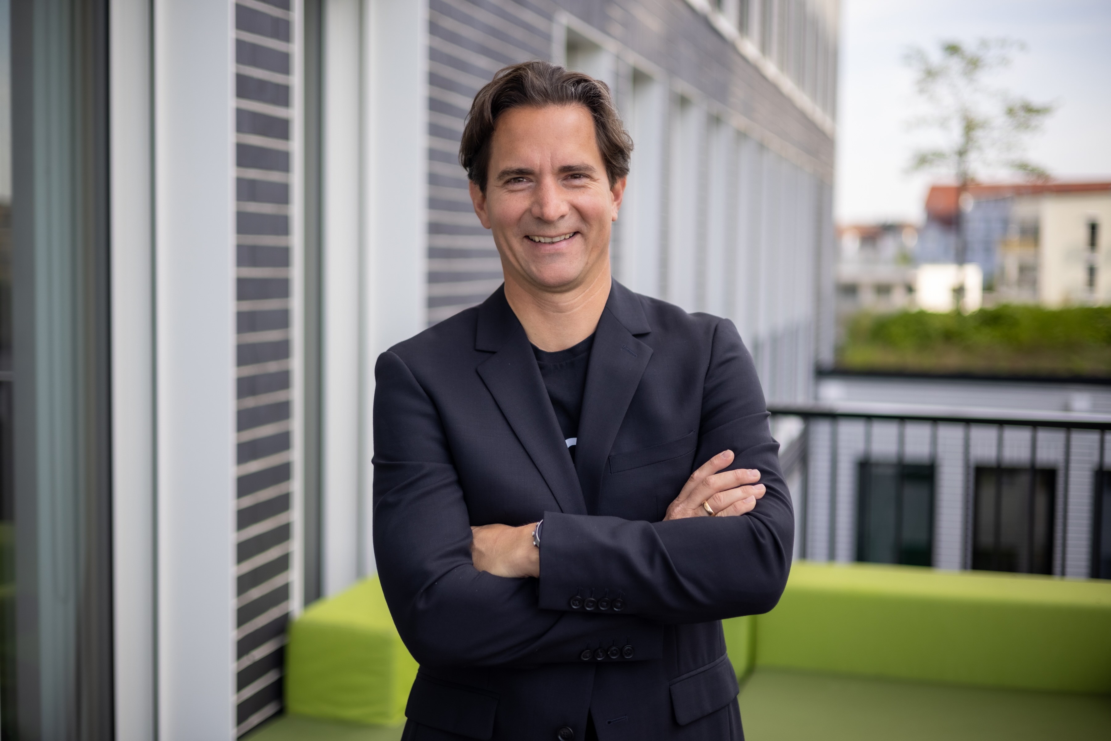 Mann in dunklem Sakko mit verschränkten Armen lächelt in Kamera